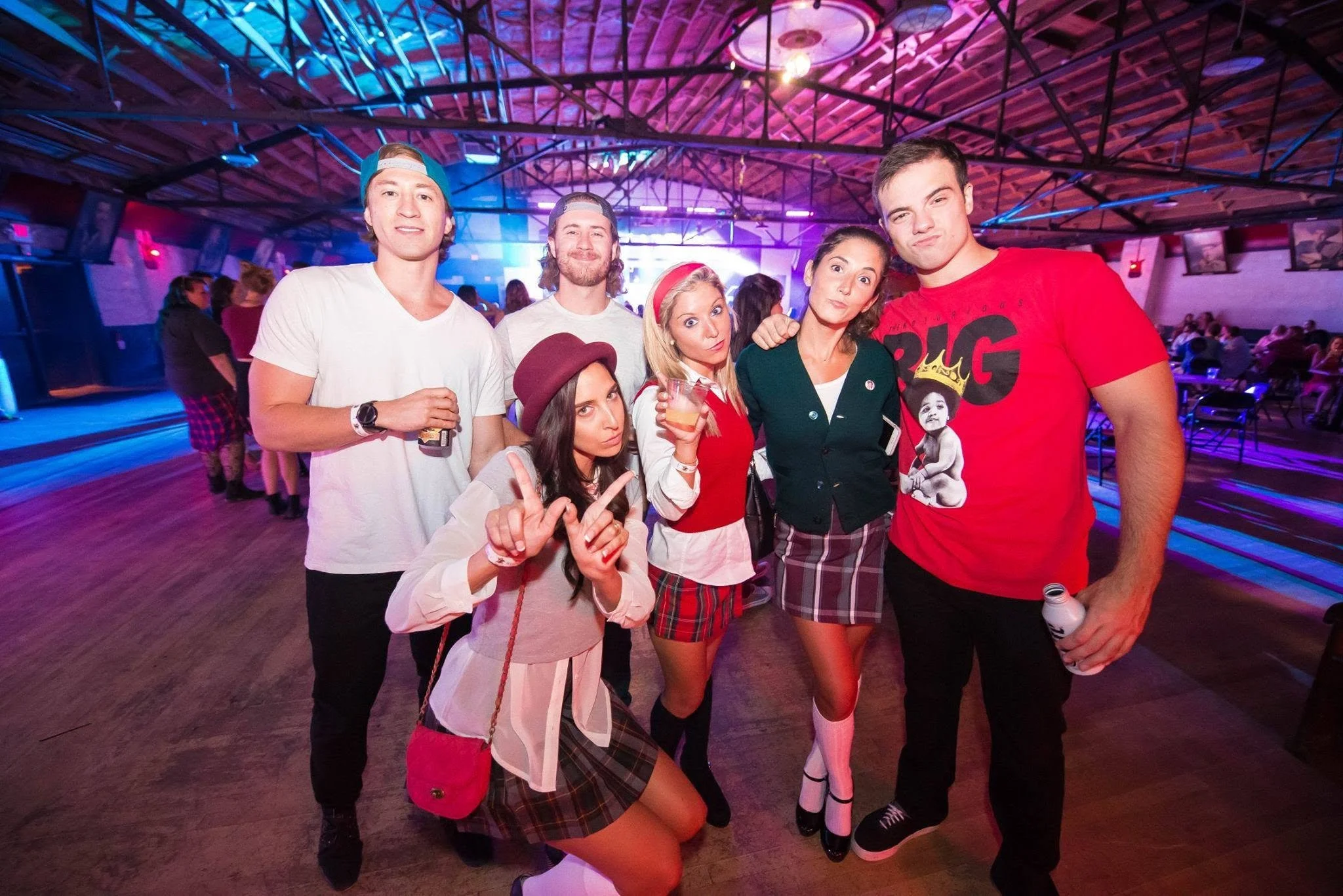 Group of young people at a party, posing for a photo with colorful lighting in the background.