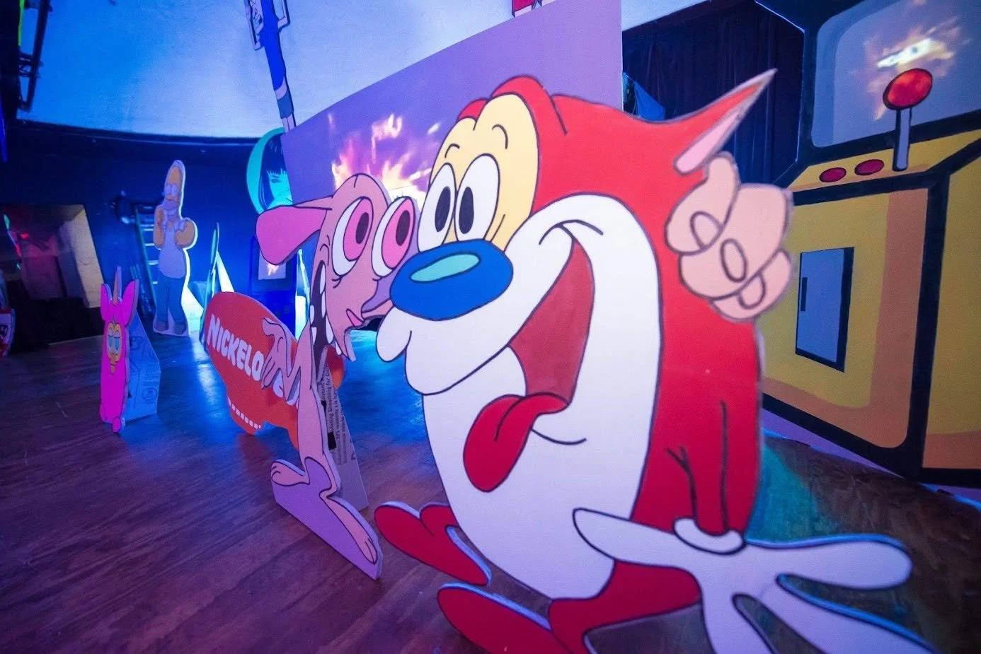 Colorful display of cartoon characters from Nickelodeon, including a cheerful red and white cat and pink dog, with a background of arcade game themed decorations.
