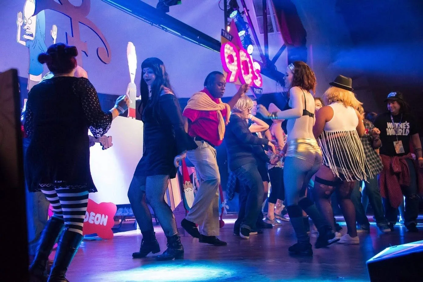 People dancing on a stage during a party with colorful decorations and signs.