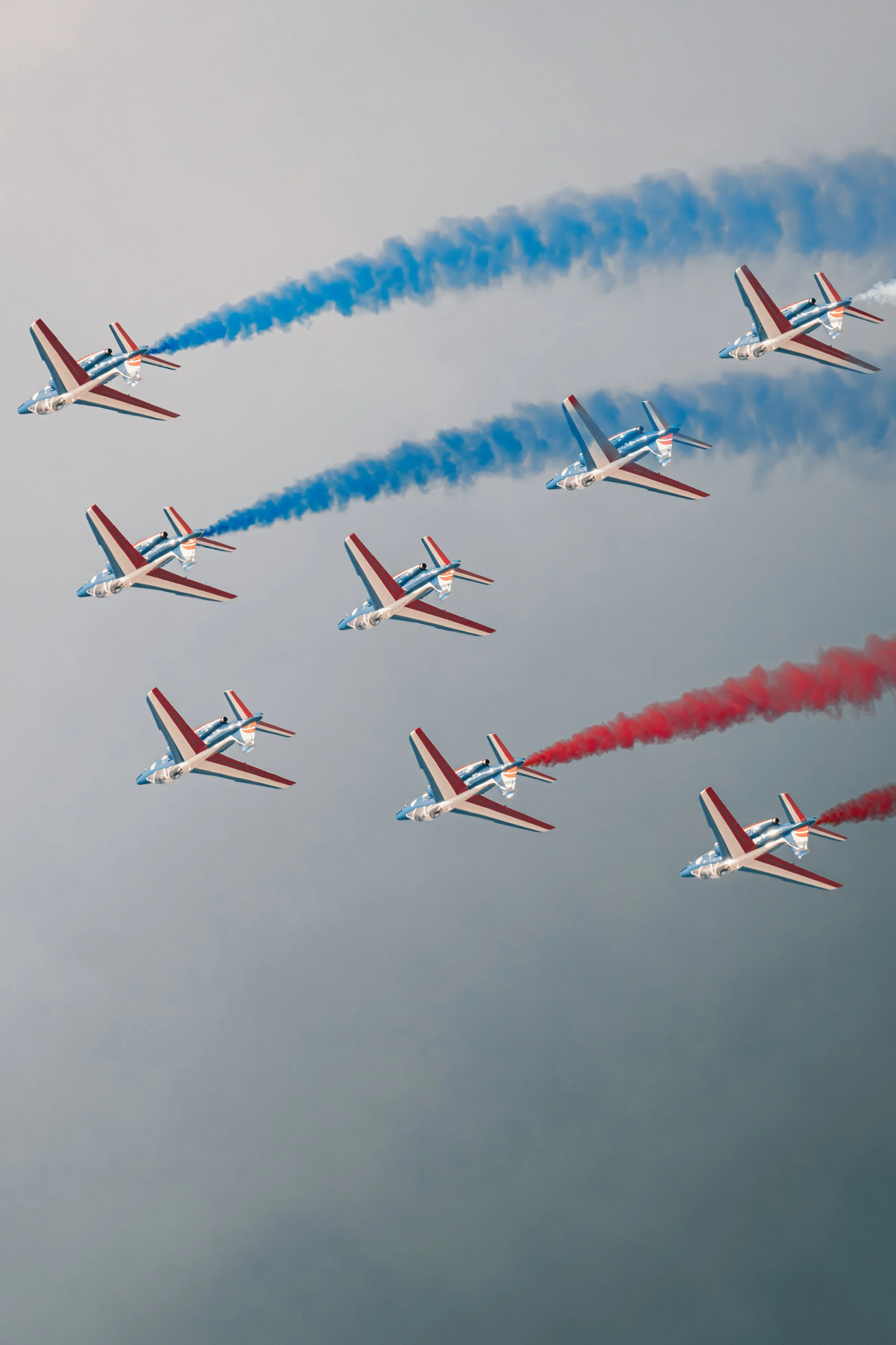 Huit avions de l'équipe acrobatique française Patrouille de France en vol, formant un V, laissant derrière eux des traînées de fumée bleue, blanche et rouge.