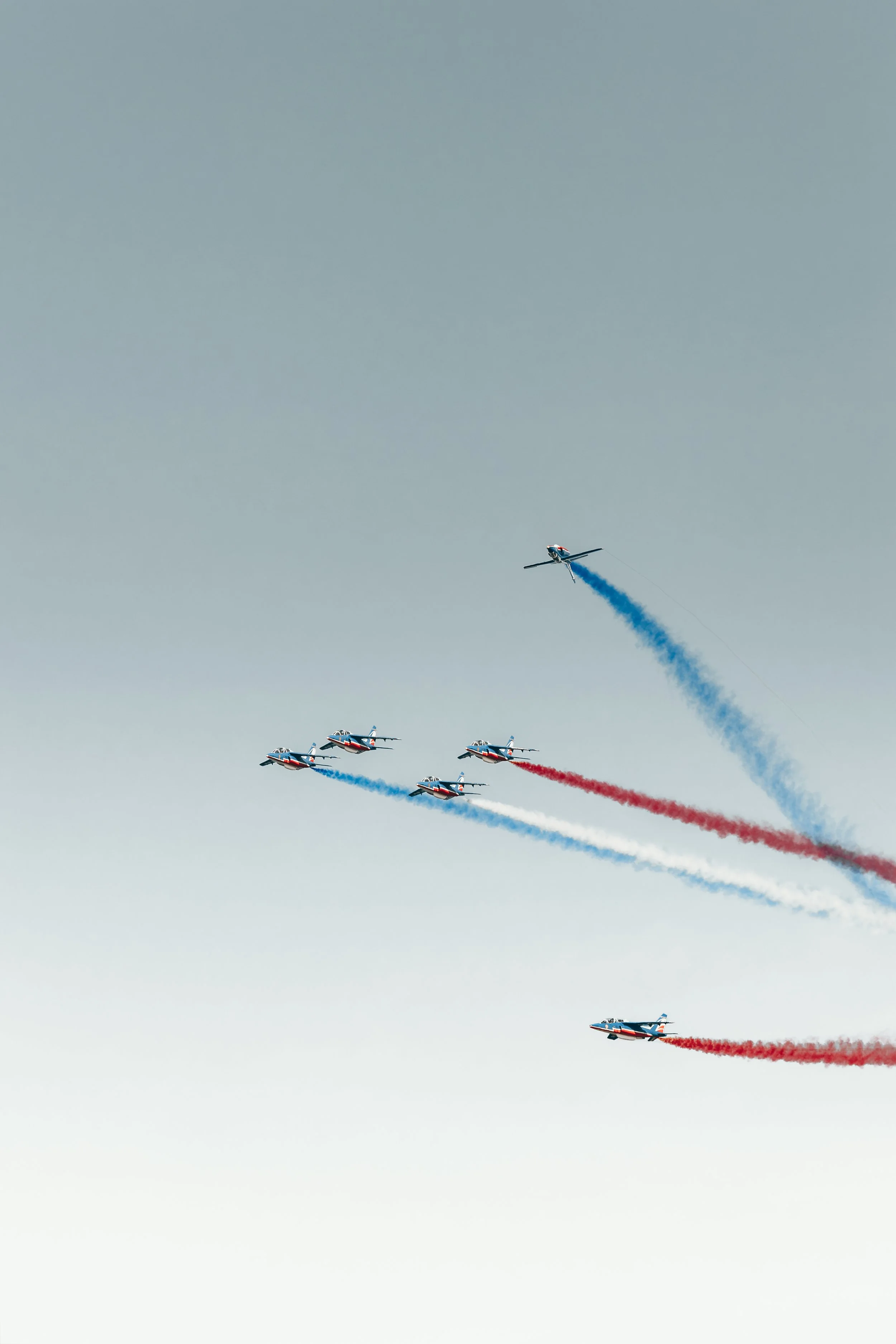 Série d'avions de chasse effectuant une acrobatie aérienne avec des traînées de fumée rouge, blanche et bleue dans le ciel.