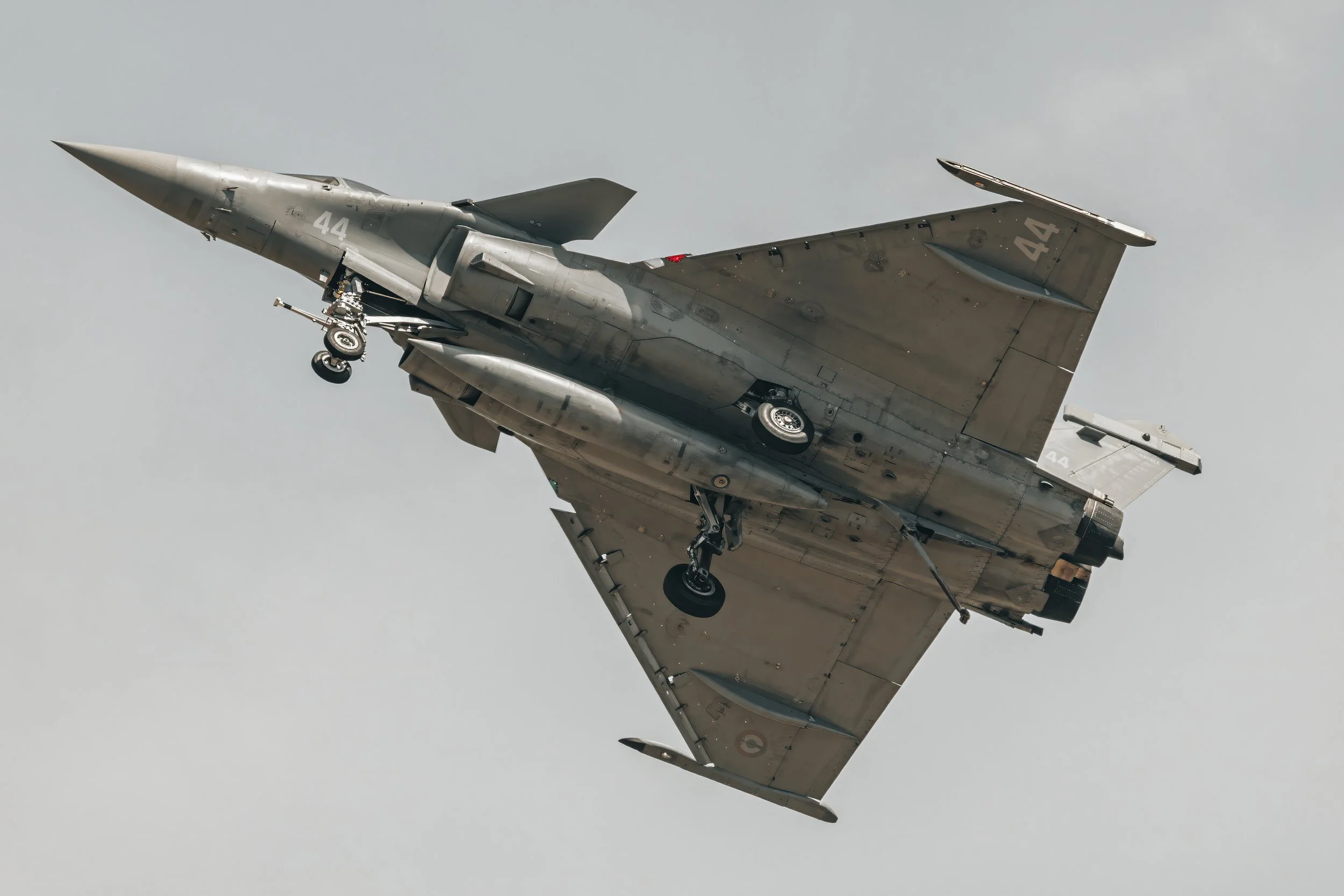 Avion de chasse en vol avec le train d'atterrissage partiellement sorti, ciel gris en arrière-plan.