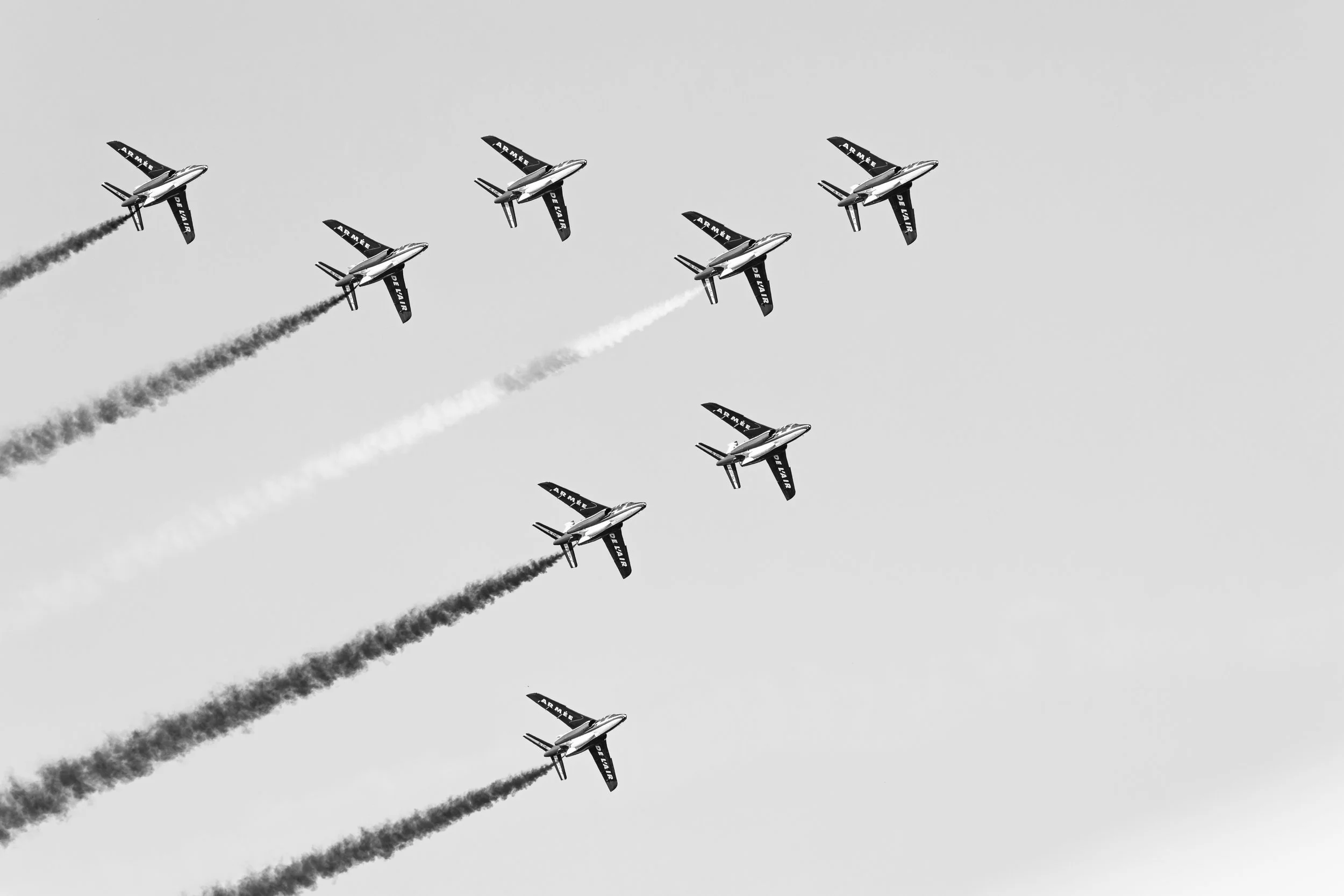 Vingt-quatre avions de combat volent en formation, laissant des traînées de fumée. L'image est en noir et blanc.