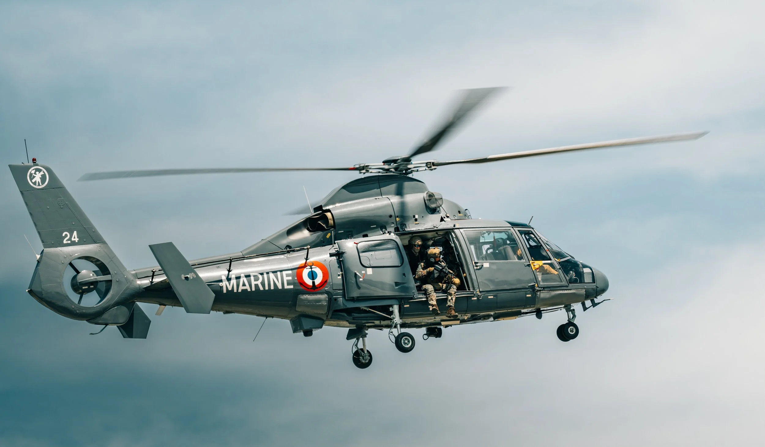Un hélicoptère militaire avec plusieurs soldats à l'intérieur, en vol contre un ciel nuageux.