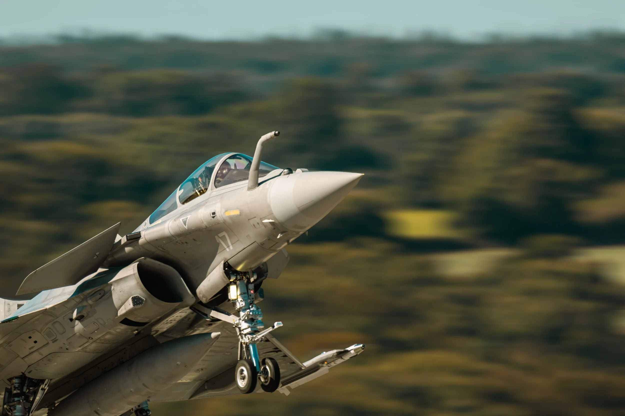 Avion de chasse en vol, vue rapprochée du nez et du cockpit, fond flou.