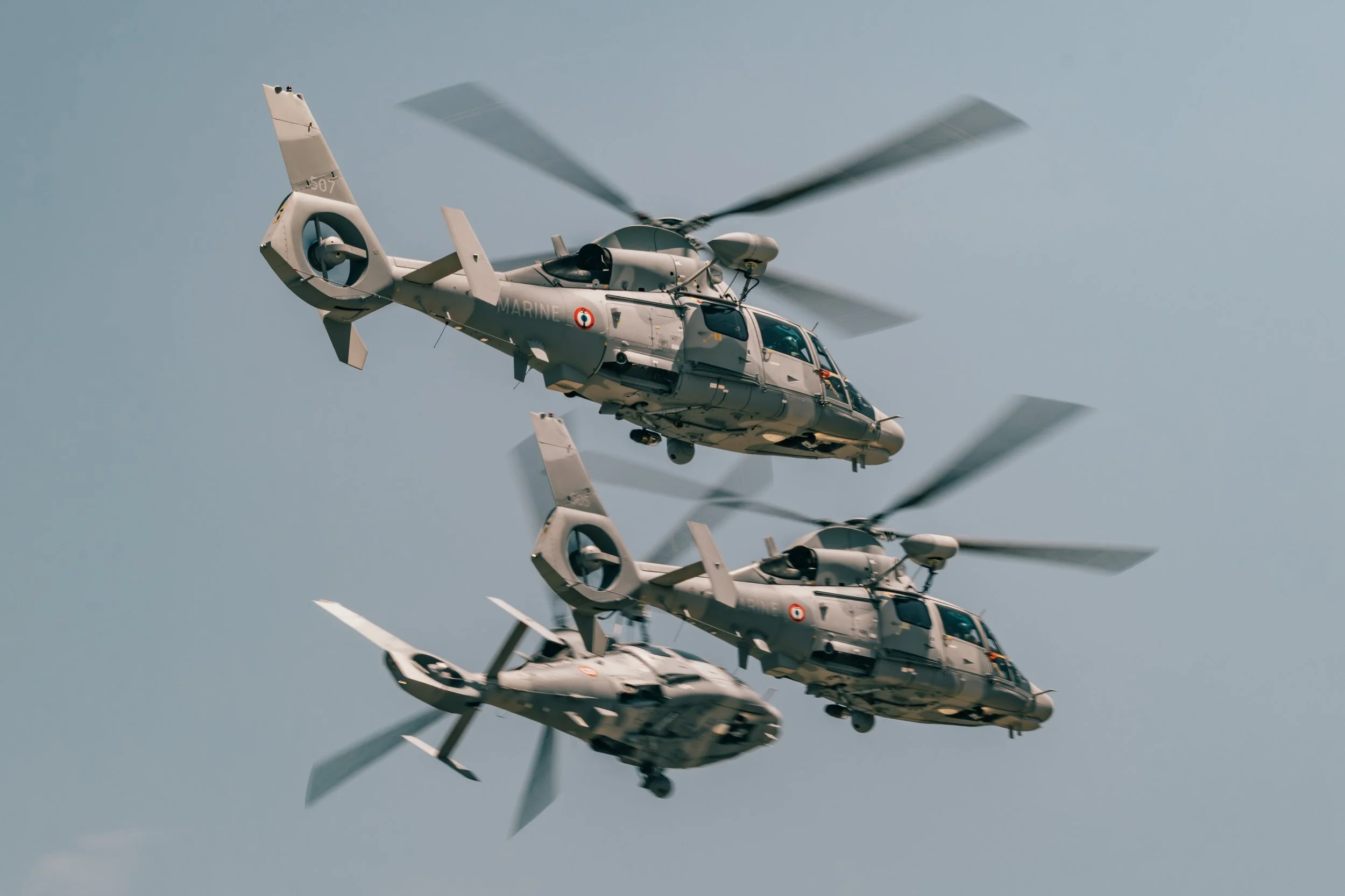 Trois hélicoptères militaires volants en formation dans un ciel clair.