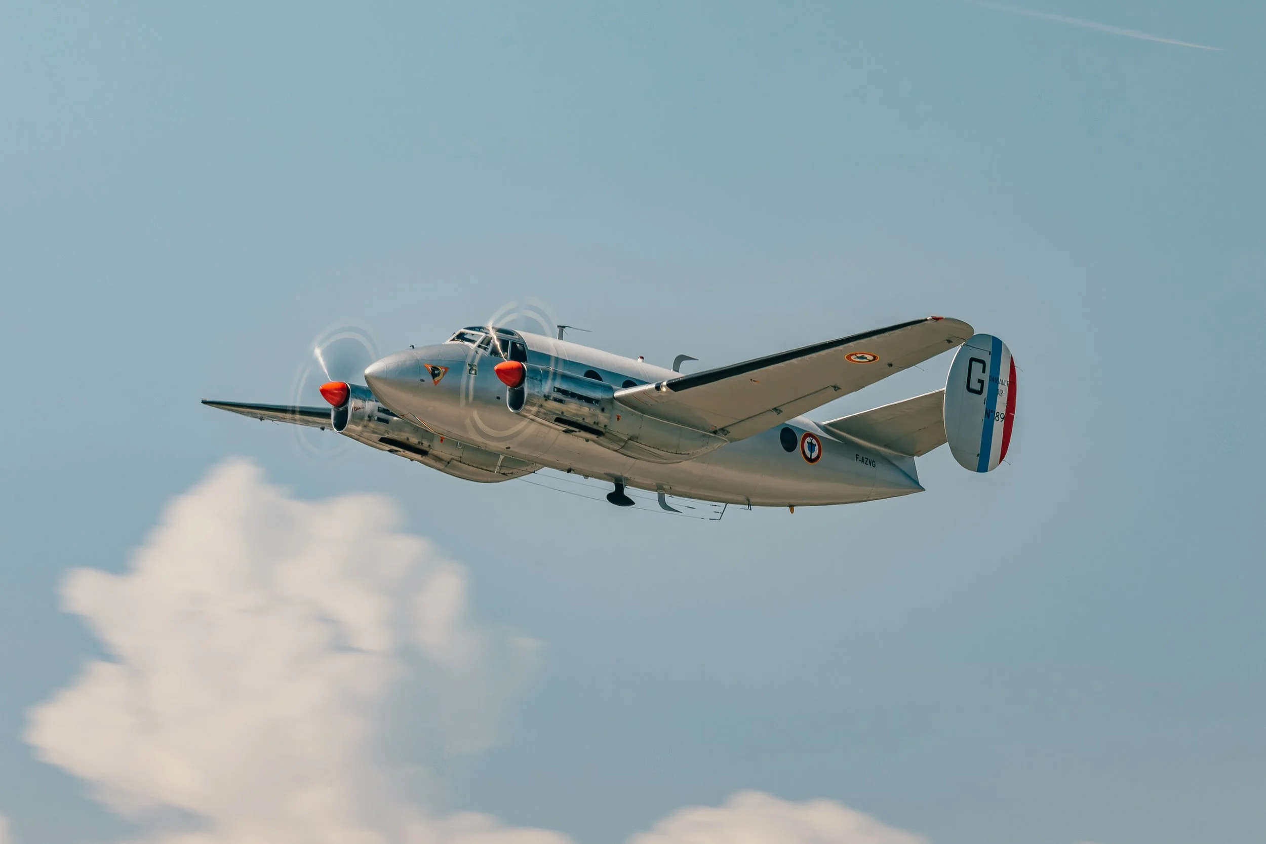 Un avion de chasse en vol dans le ciel clair avec quelques nuages et une traînée blanche