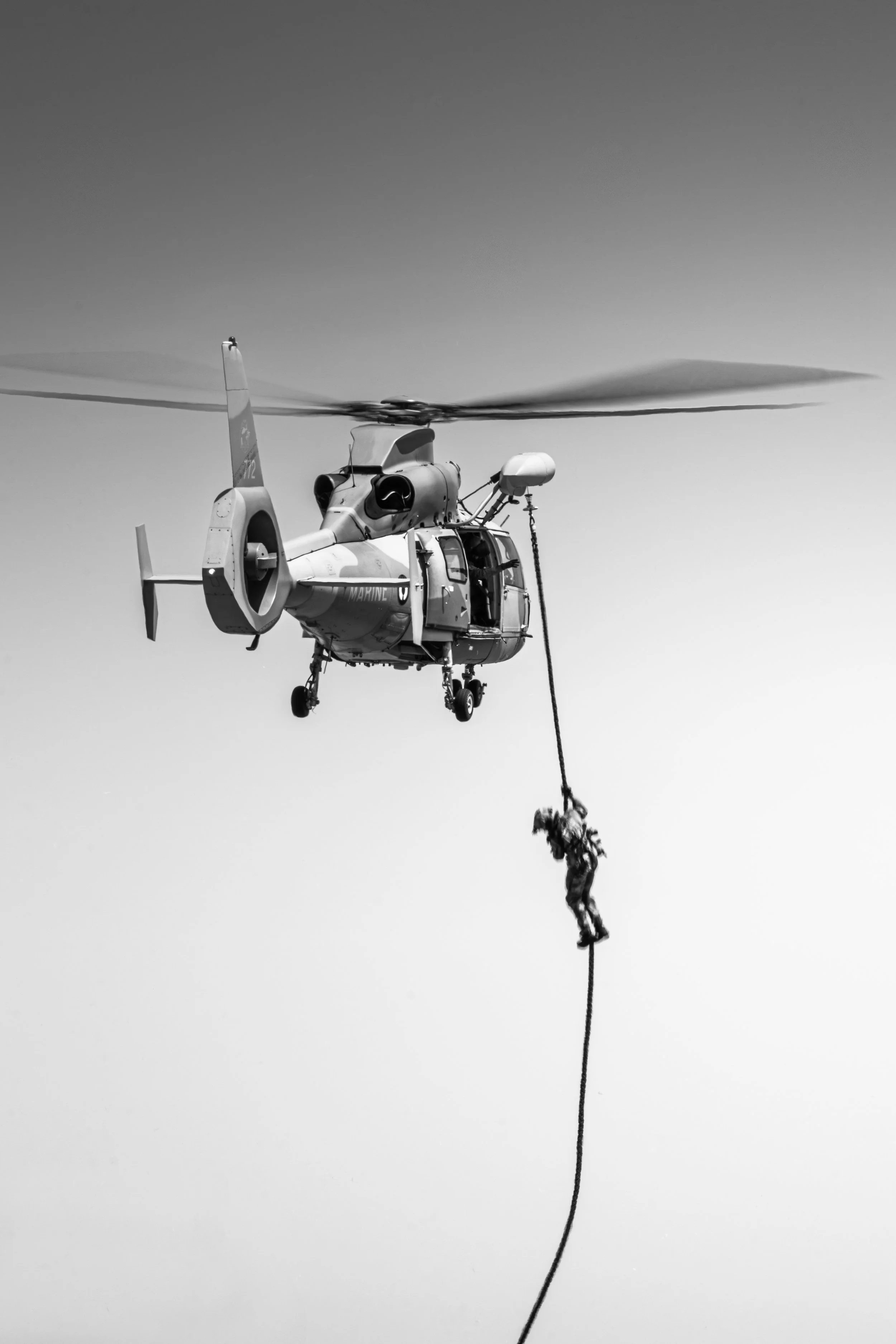 Un hélicoptère en vol avec un câble suspendant un plongeur ou un objet en dessous.