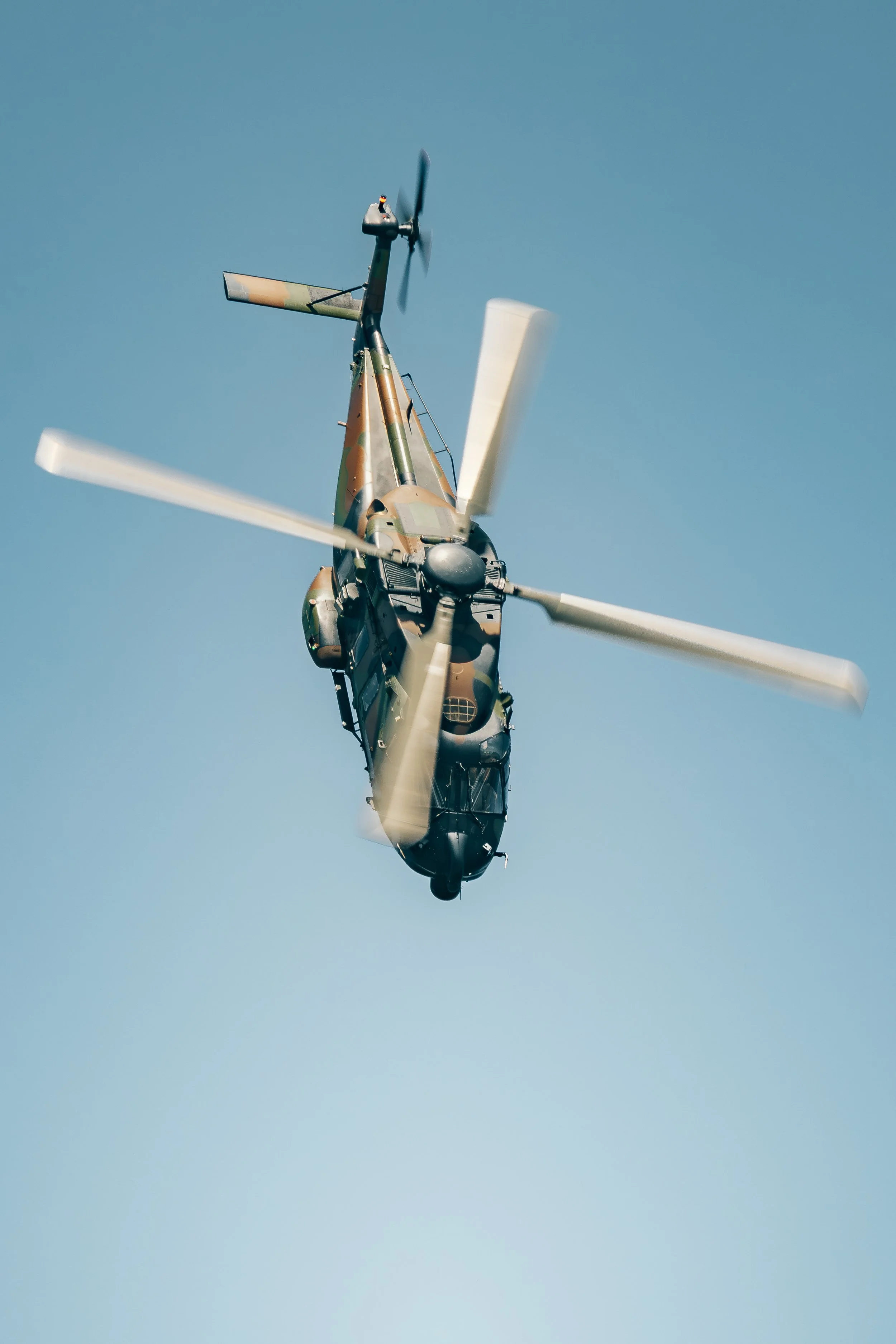 Un hélicoptère en vol vu du dessous, tournant dans un ciel clair.