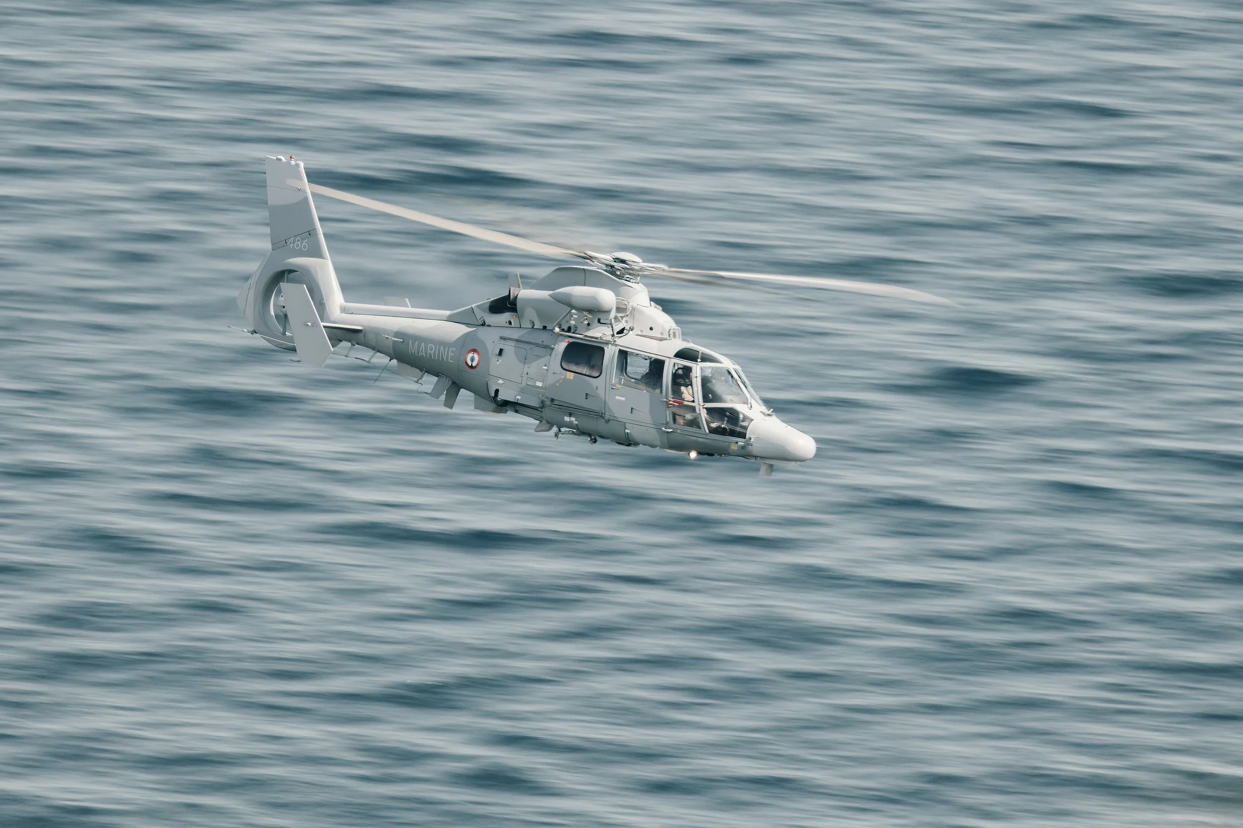 Un hélicoptère blanc vol dans une mer calme.