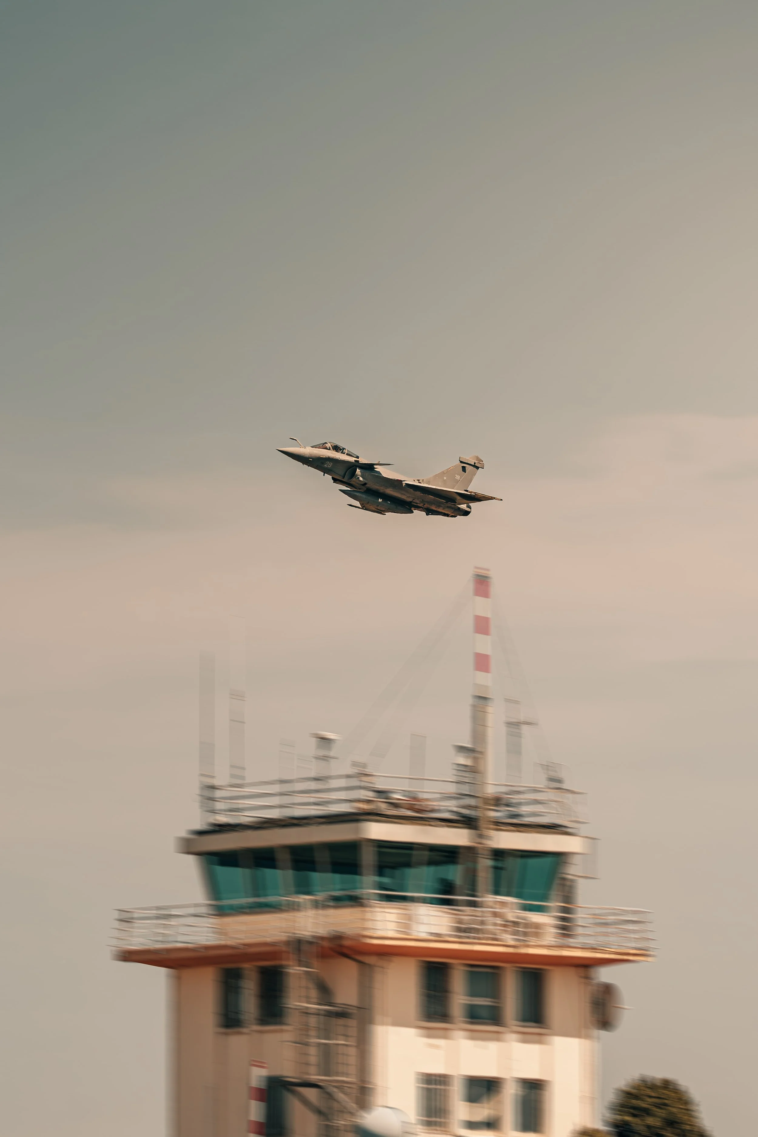 Un avion de chasse passe au-dessus d'une tour de contrôle d'aéroport.