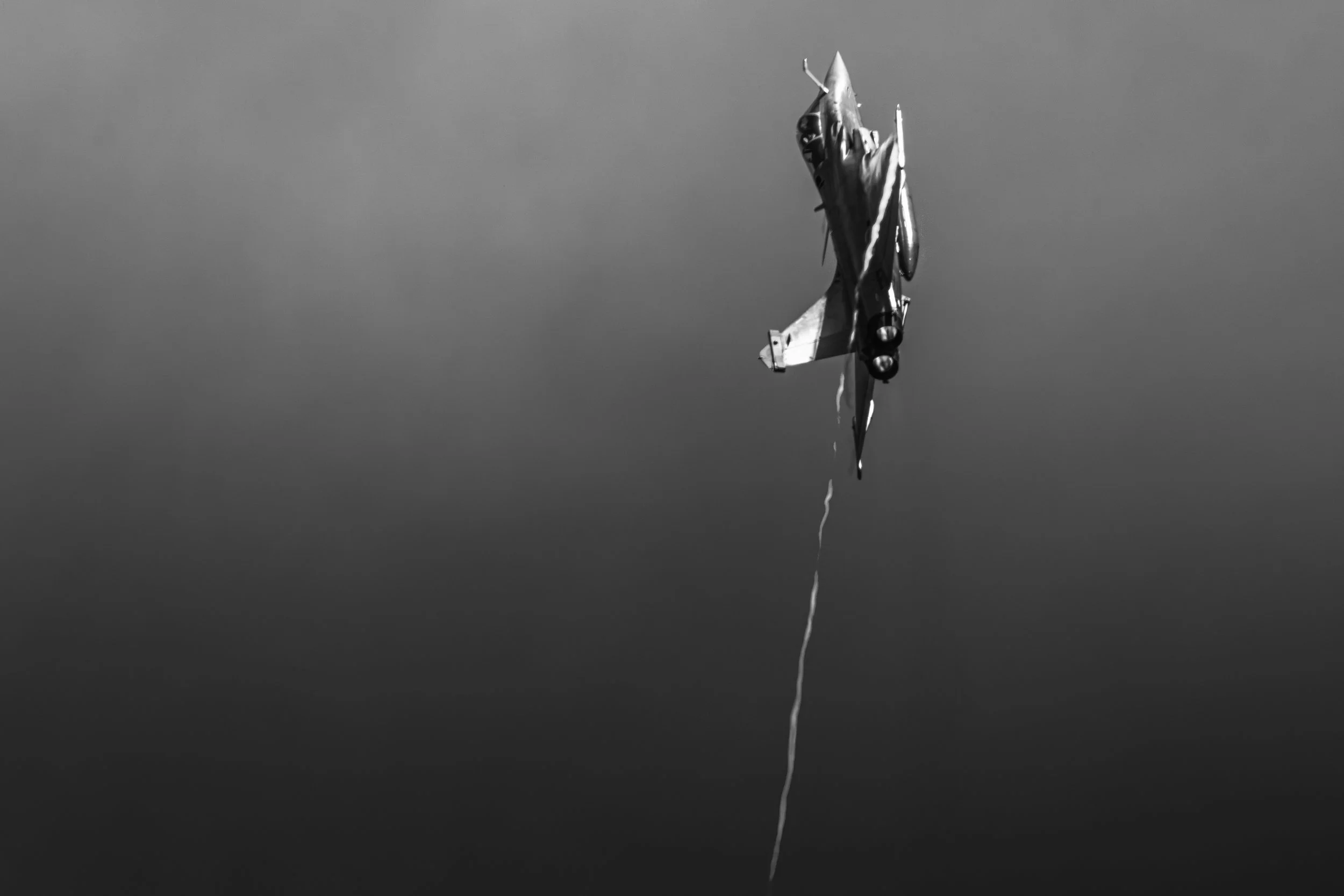 Un avion de chasse en vol biplan, vu en noir et blanc avec un reflet dans l'eau en dessous.