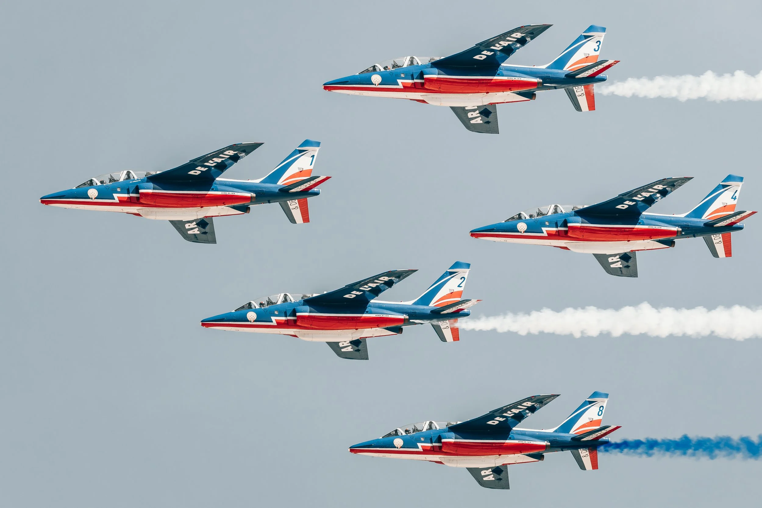 Un peloton de jets de l'Armée de l'air française en vol en formation, déployant des traînées de fumée blanche dans un ciel dégagé.