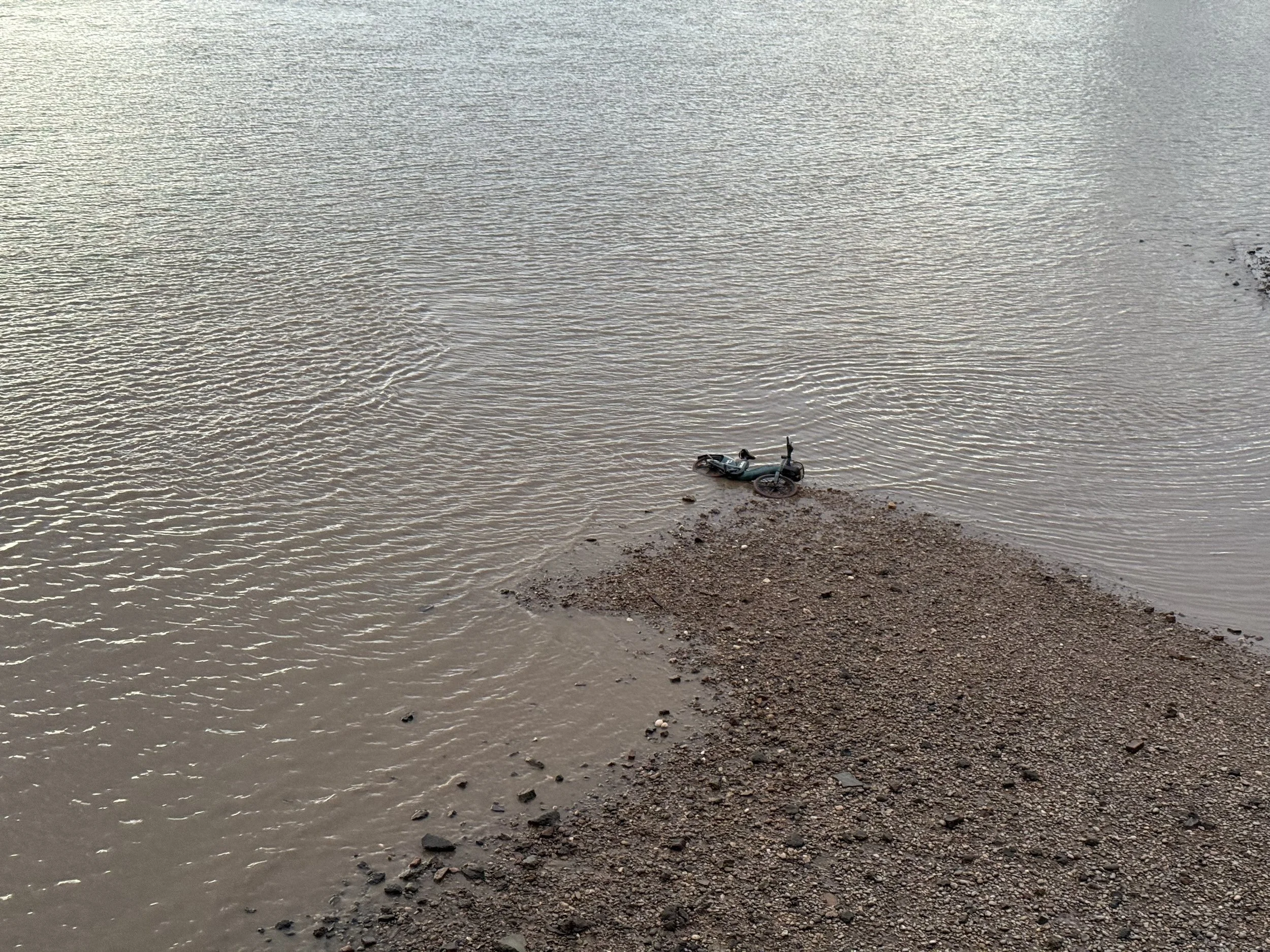 A bicycle resting on a narrow strip of rocky land beside a large body of water with gentle ripples.