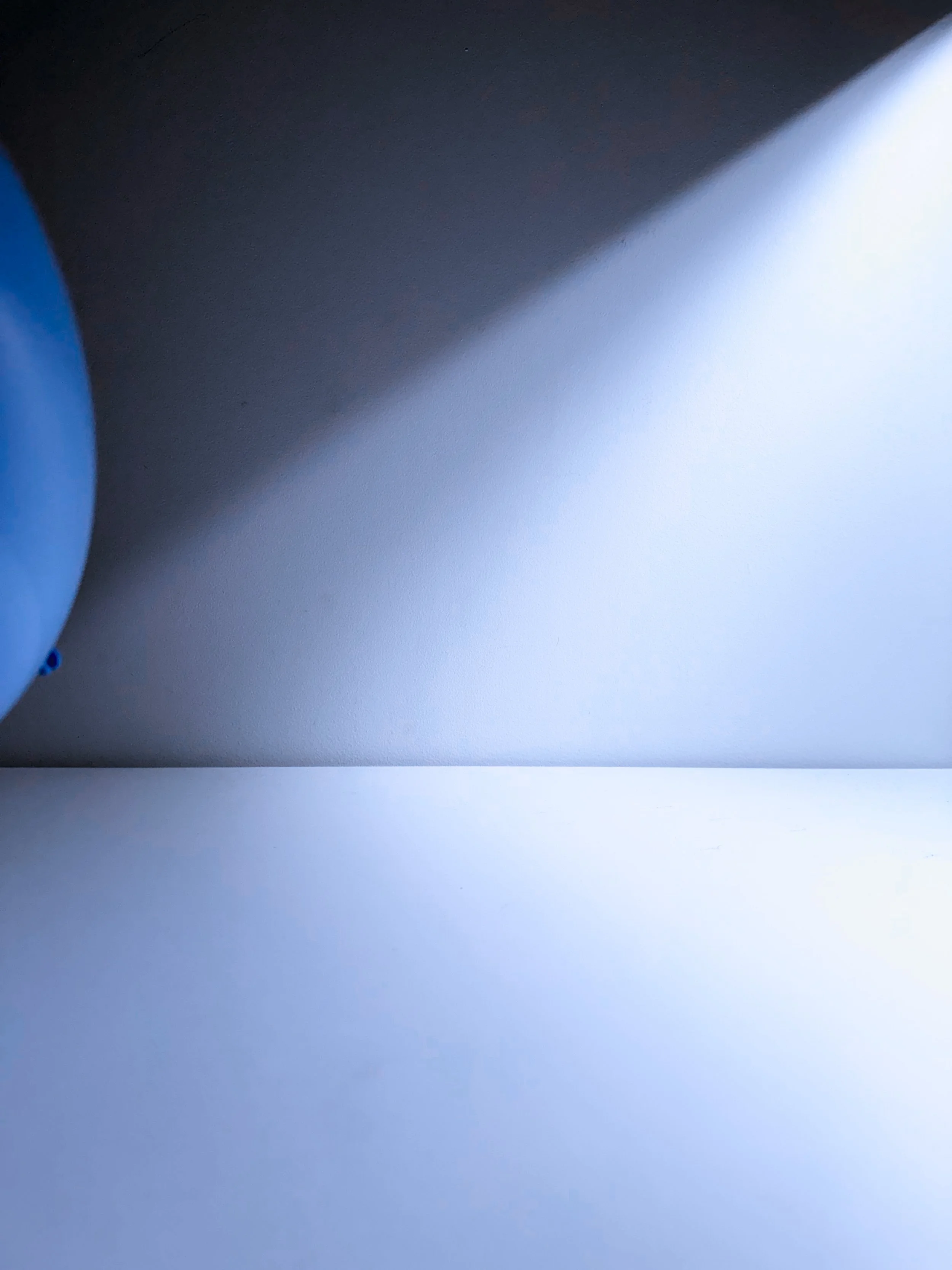 Close-up of a white wall with a shadow cast across it, part of a blue object on the left side, and a bright light source on the right.