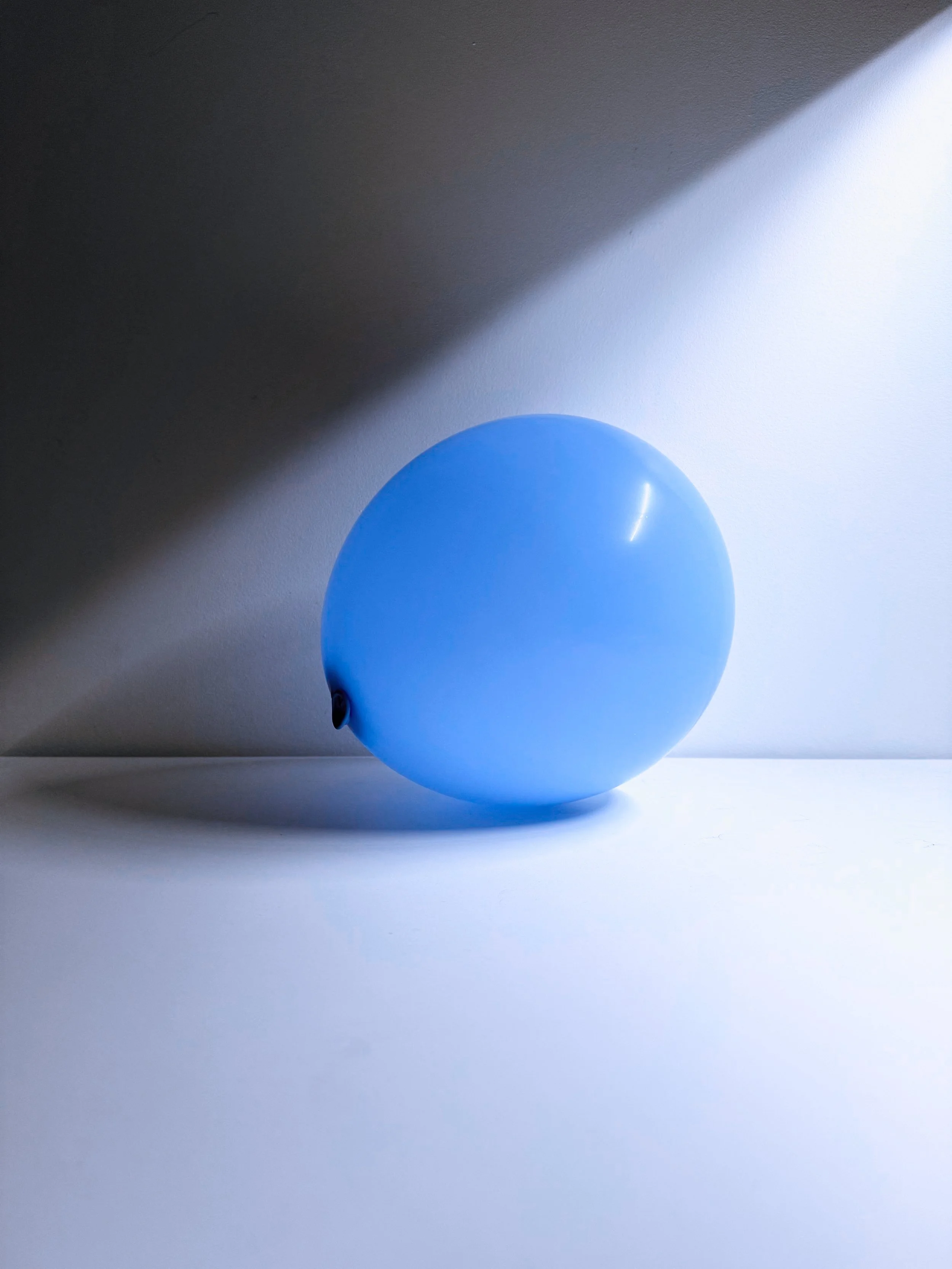 A single blue balloon on a white surface with a shadow cast on the wall behind.
