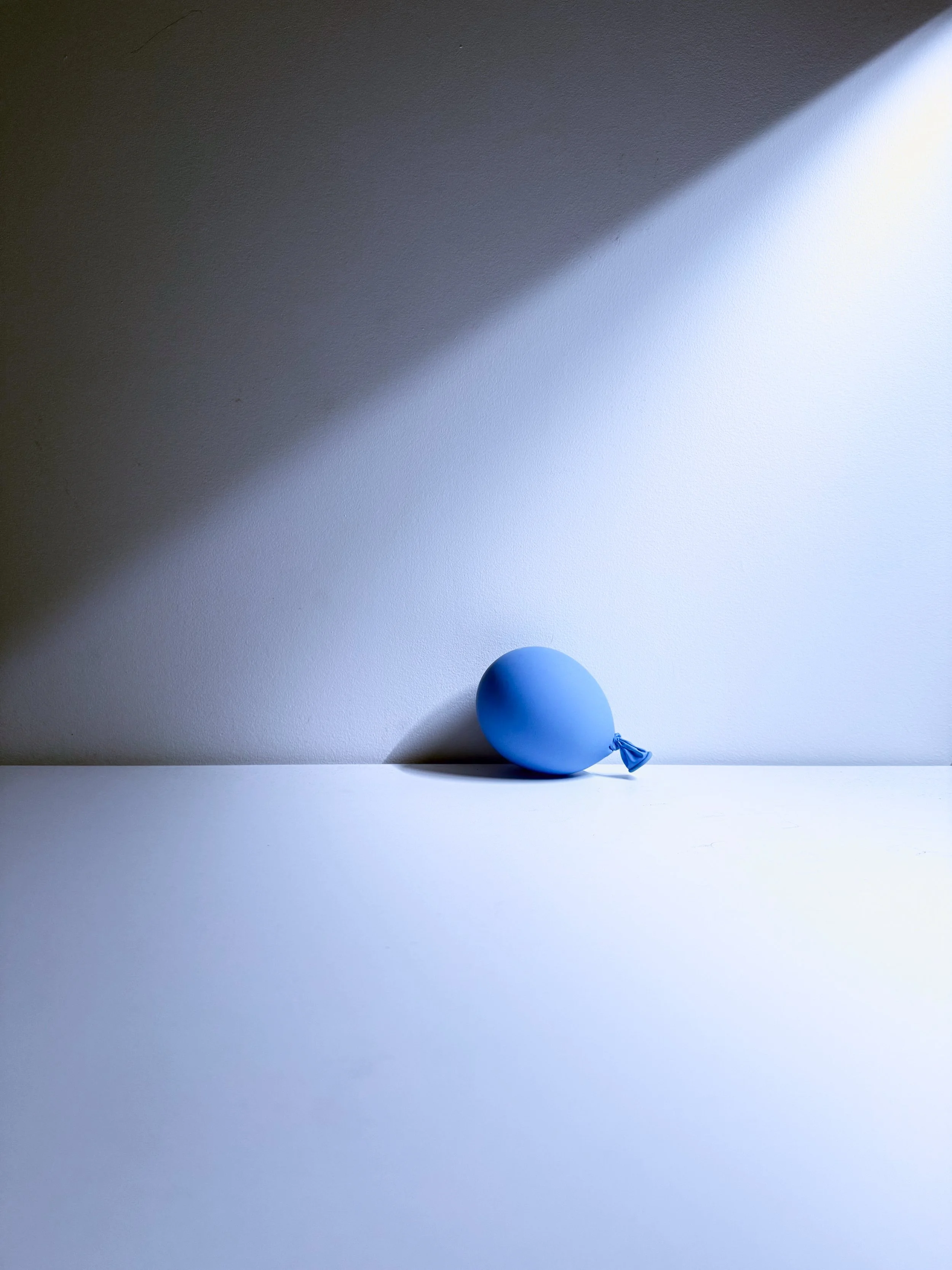 A blue balloon tied with a string on a white surface with a shadow and a dark ceiling above.