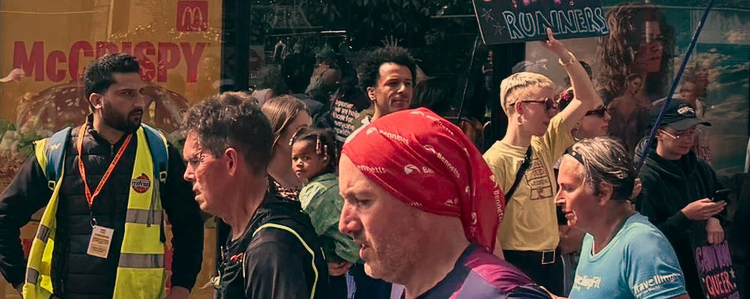 A group of diverse runners participating in a race, some wearing colorful athletic clothing and headgear, with people and signs in the background.