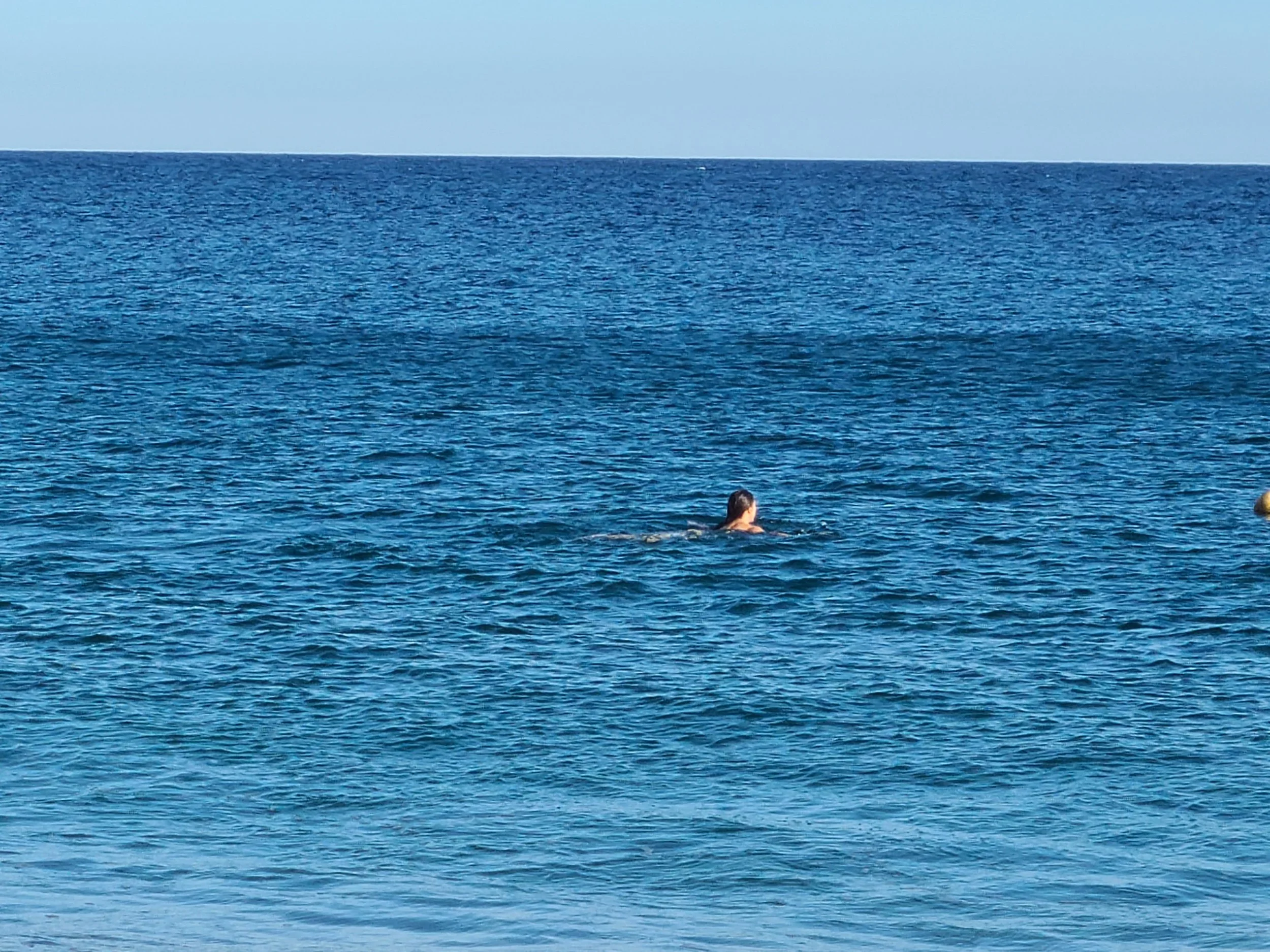 Person swimming in the ocean near a boat with a yellow and red flag.