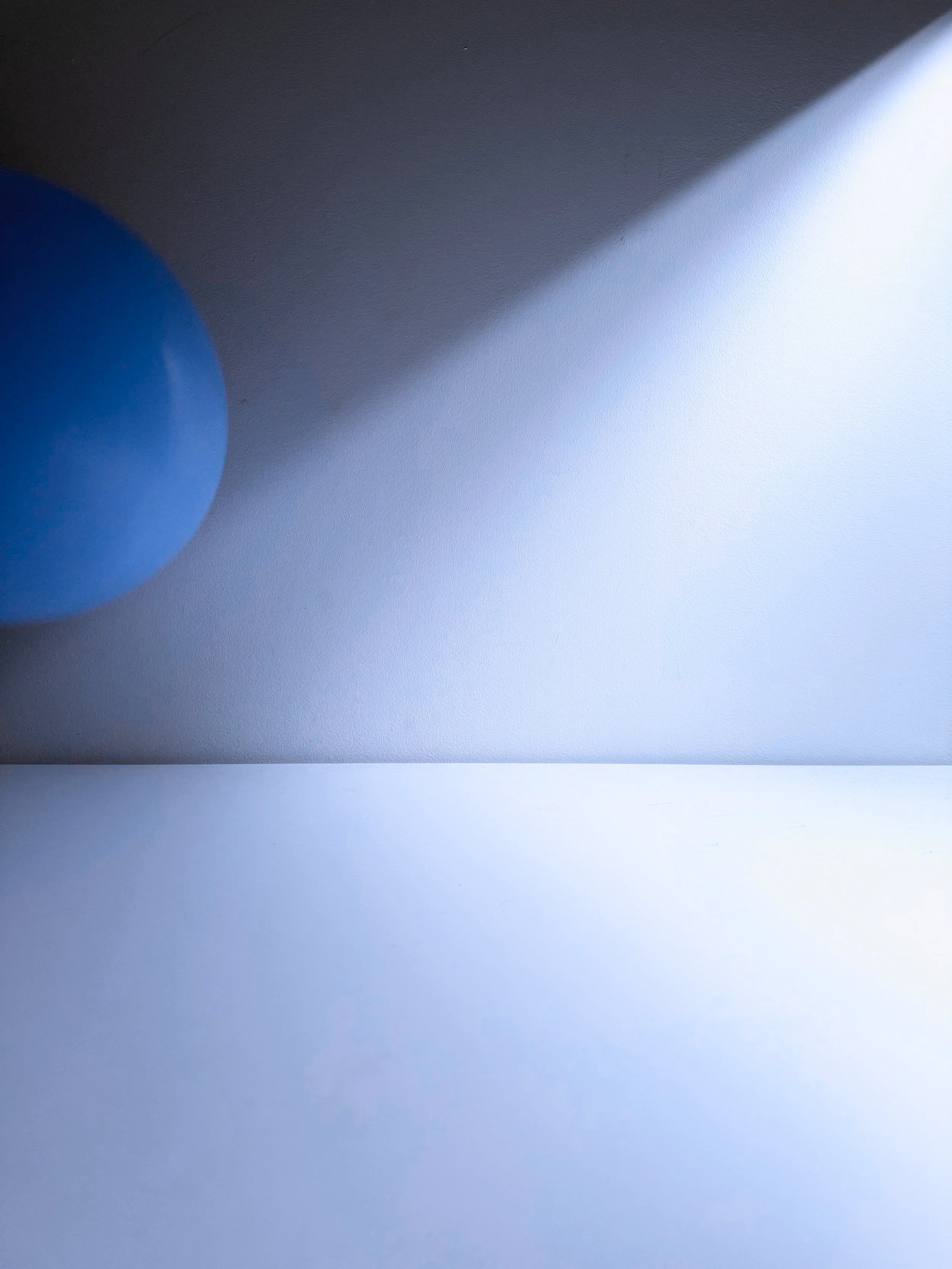 A close-up image of a blue balloon partially visible on the left and a bright white light on the right, with a shaded area in between on a smooth surface.