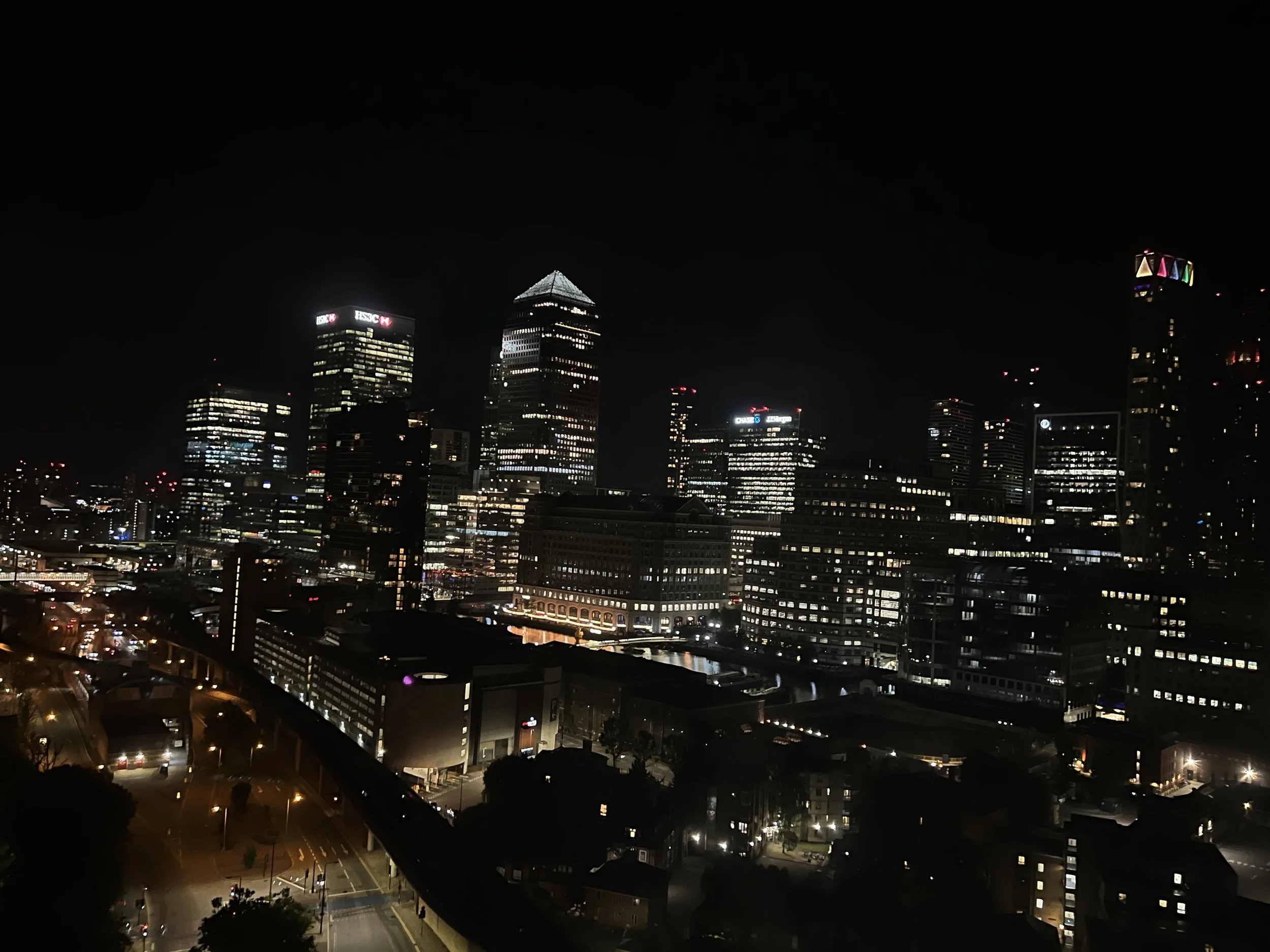 Nighttime cityscape with illuminated skyscrapers and buildings, including the HSBC building, in a modern downtown area of a city.