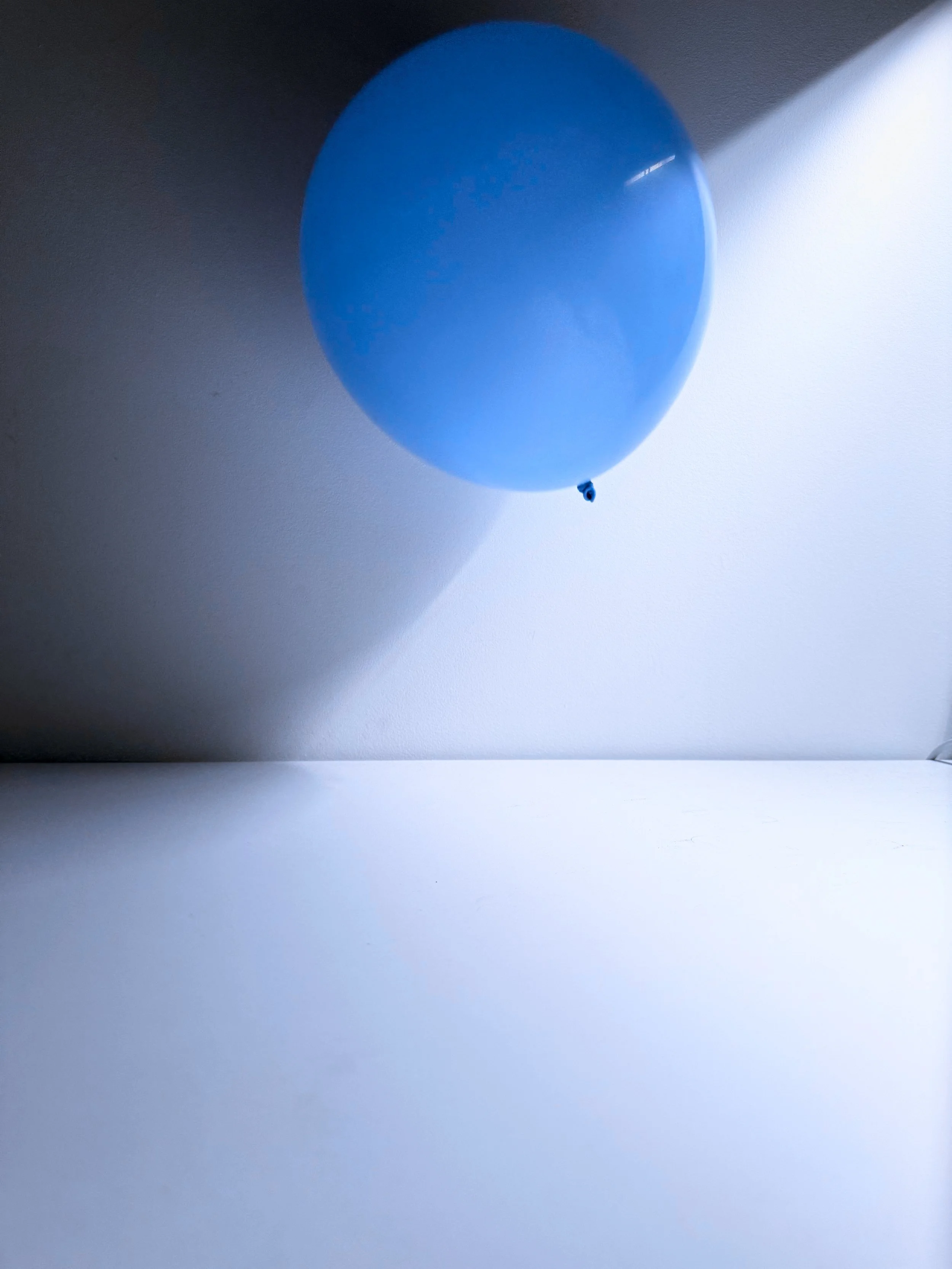 Blue balloon against a wall, casting a shadow, with a slight highlight on its surface.