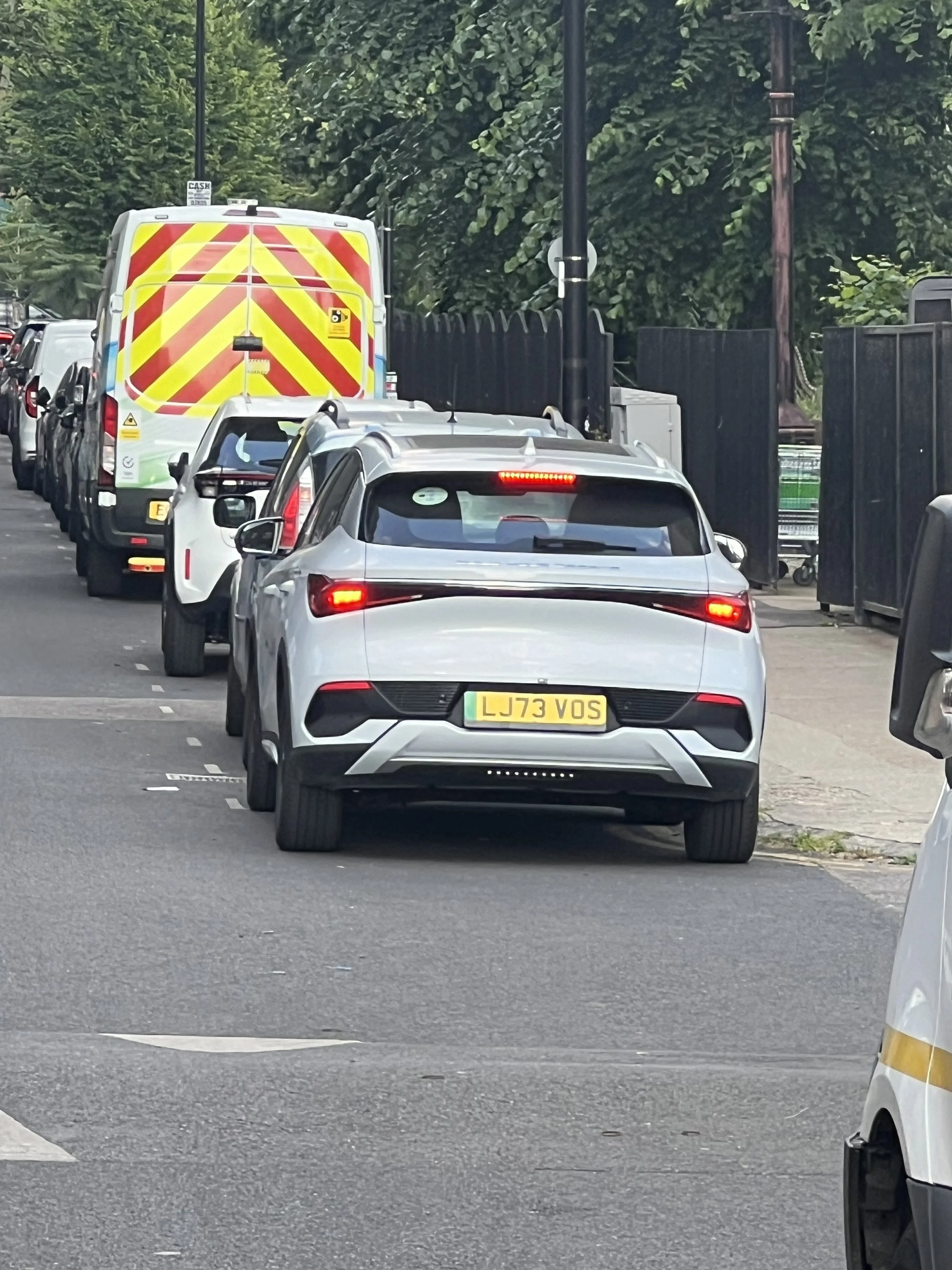 Line of parked cars on a city street with a van at the front.