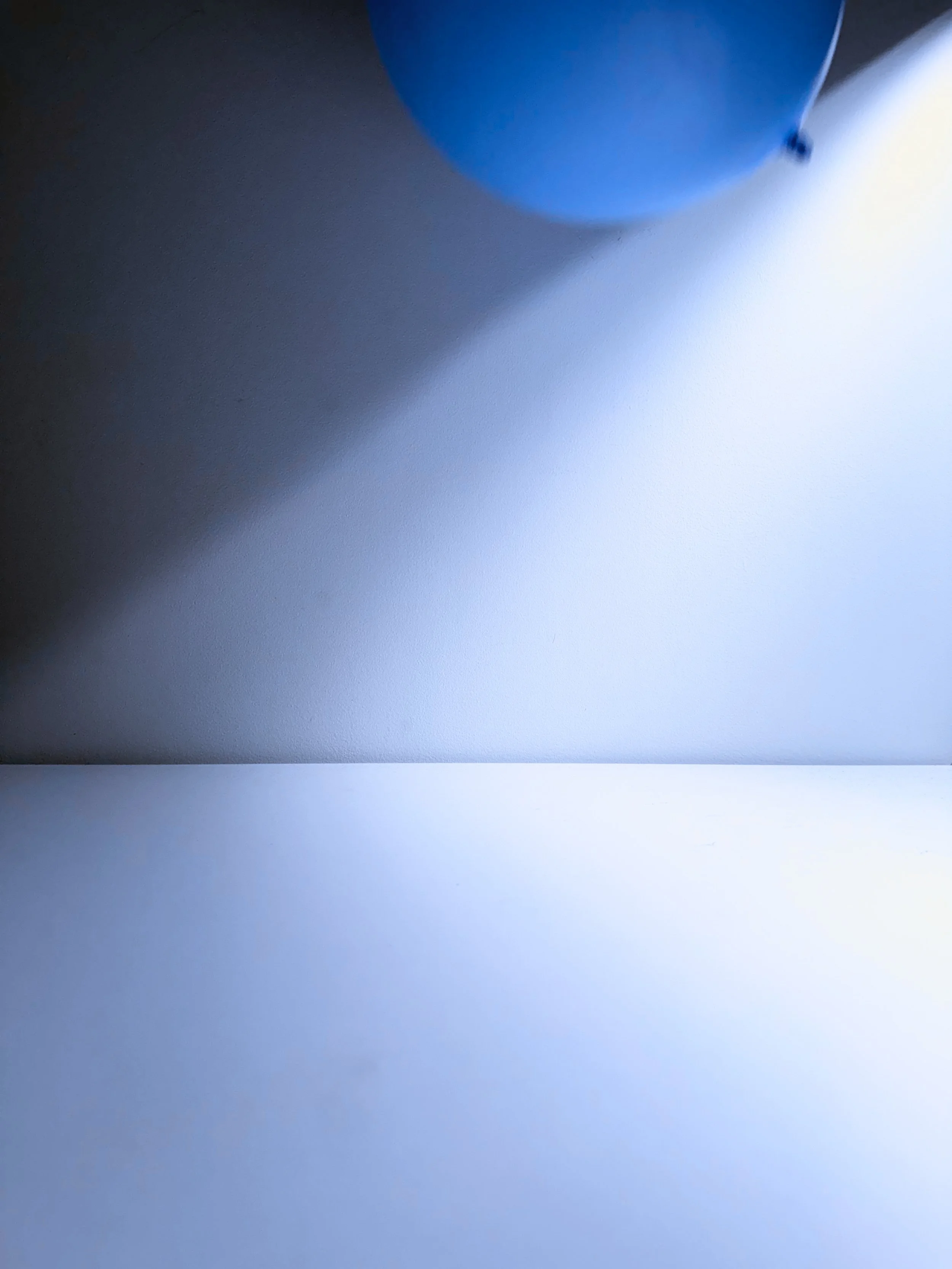 Close-up of a blue balloon casting a shadow on a white surface.