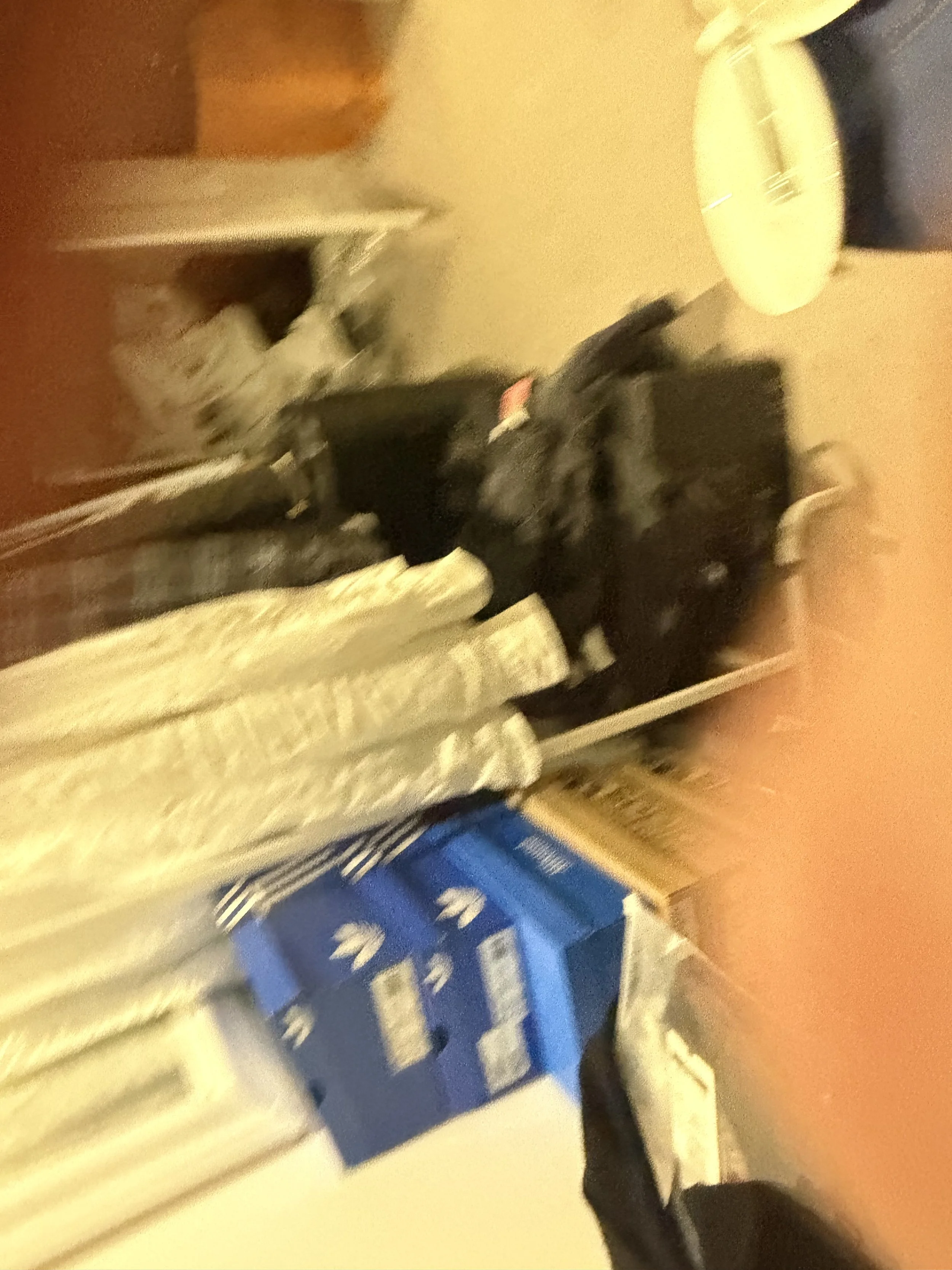 A room with various objects including a baby crib, boxes, and clothing, depicted with a yellowish-orange hue and blurry details.