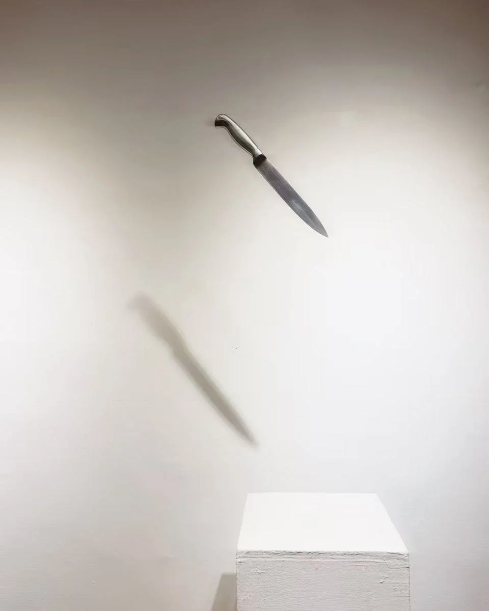 A knife appears to be floating mid-air, casting a shadow on the white background and on a white pedestal below.