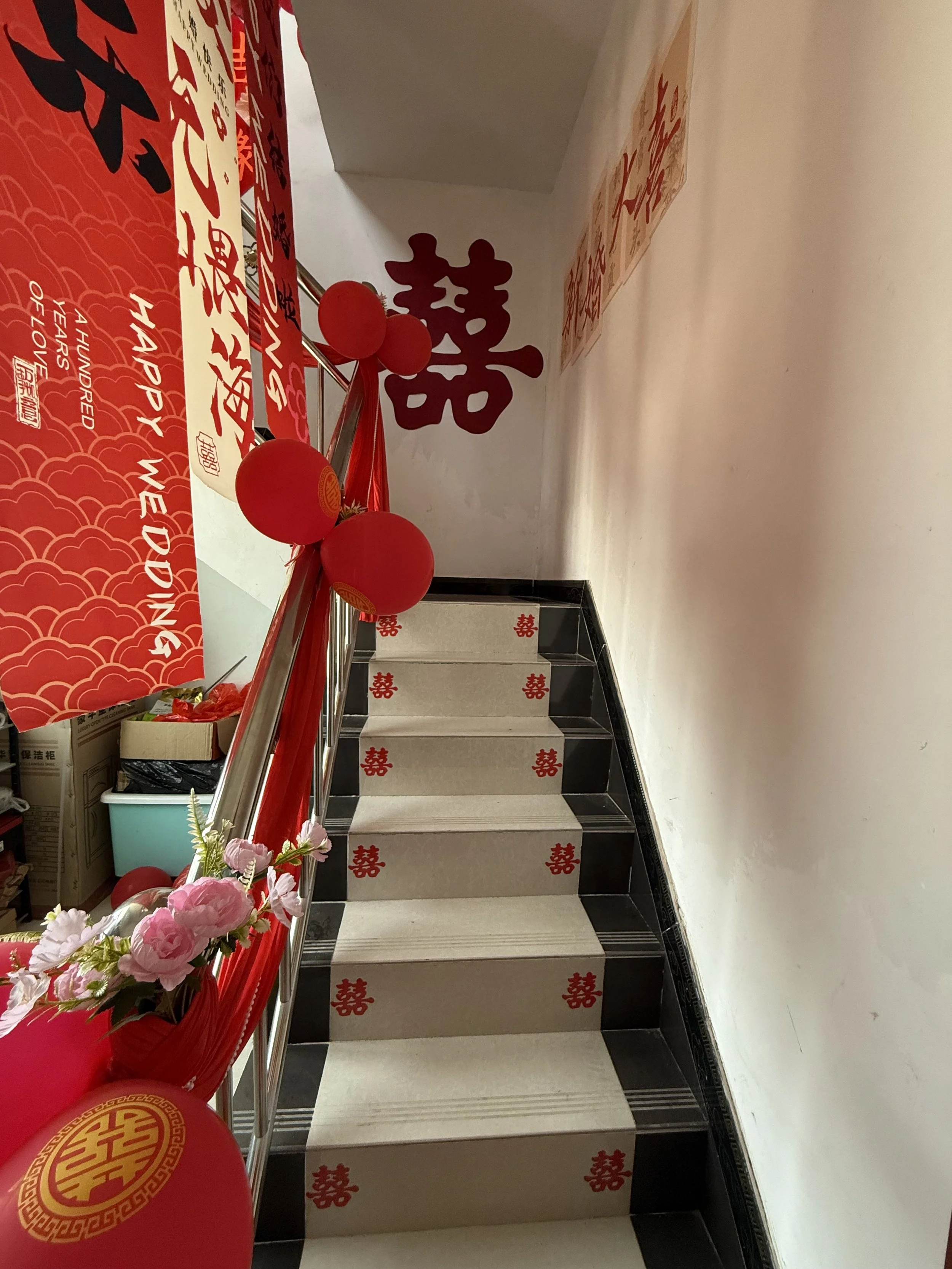 Decorated staircase with red banners, red balloons, and floral arrangements for a Chinese wedding celebration.