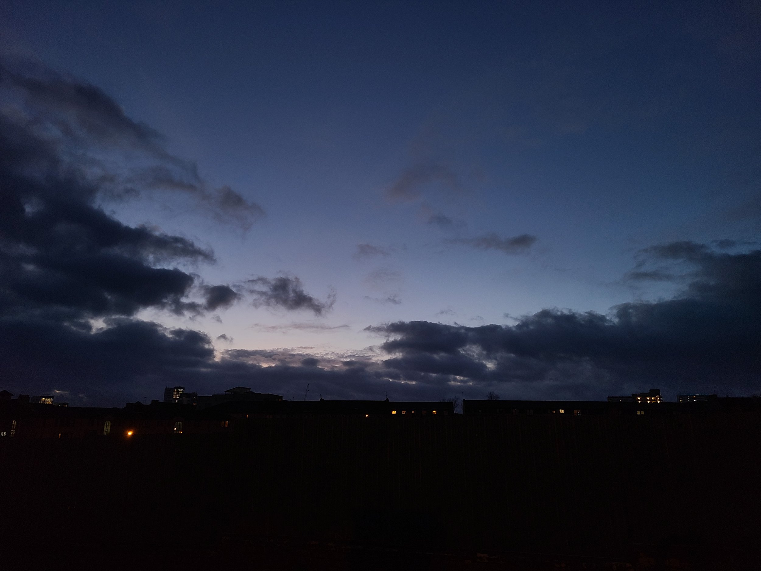 Night sky with dark clouds over a cityscape with dimly lit buildings.