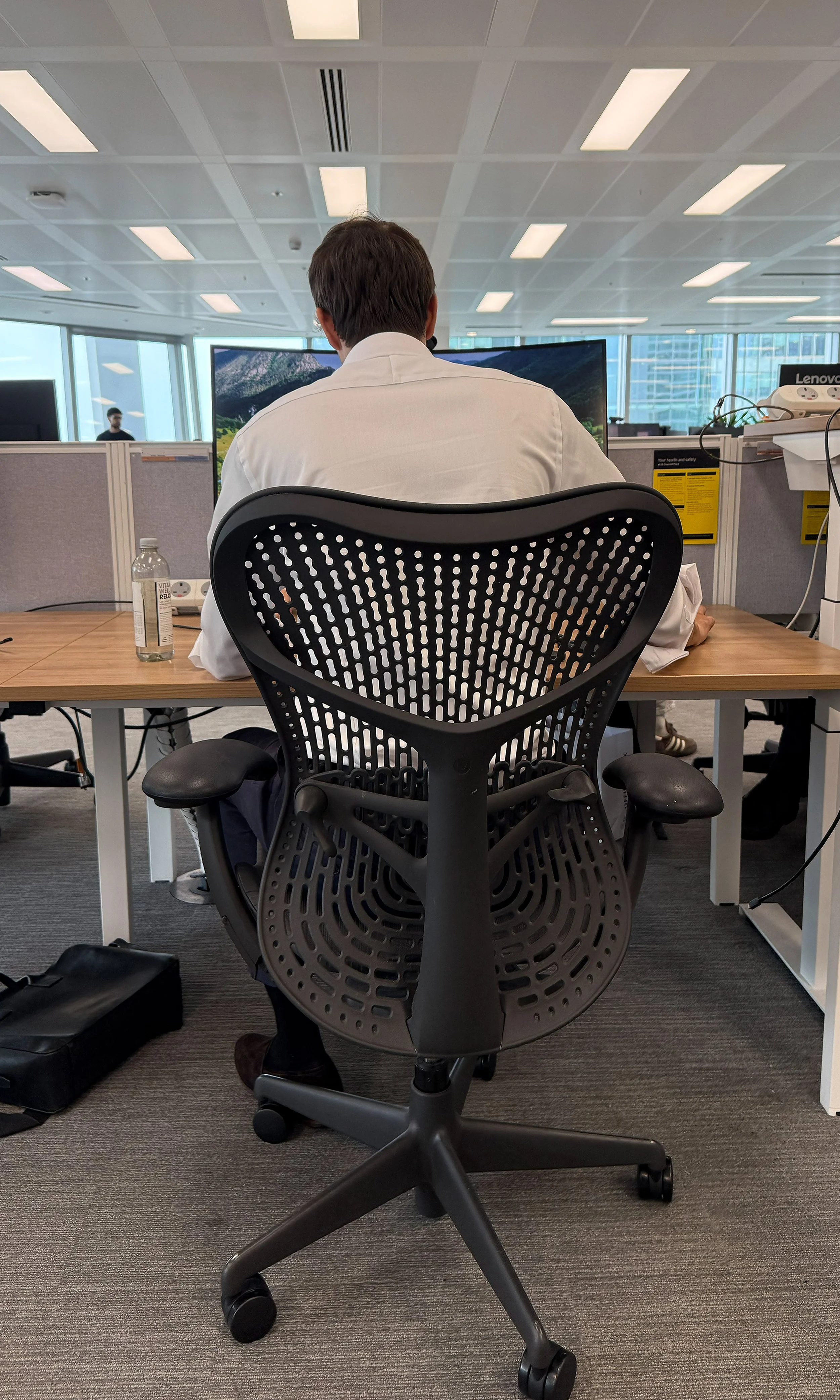 Person sitting at an office desk viewing computer screens in a modern office setting.