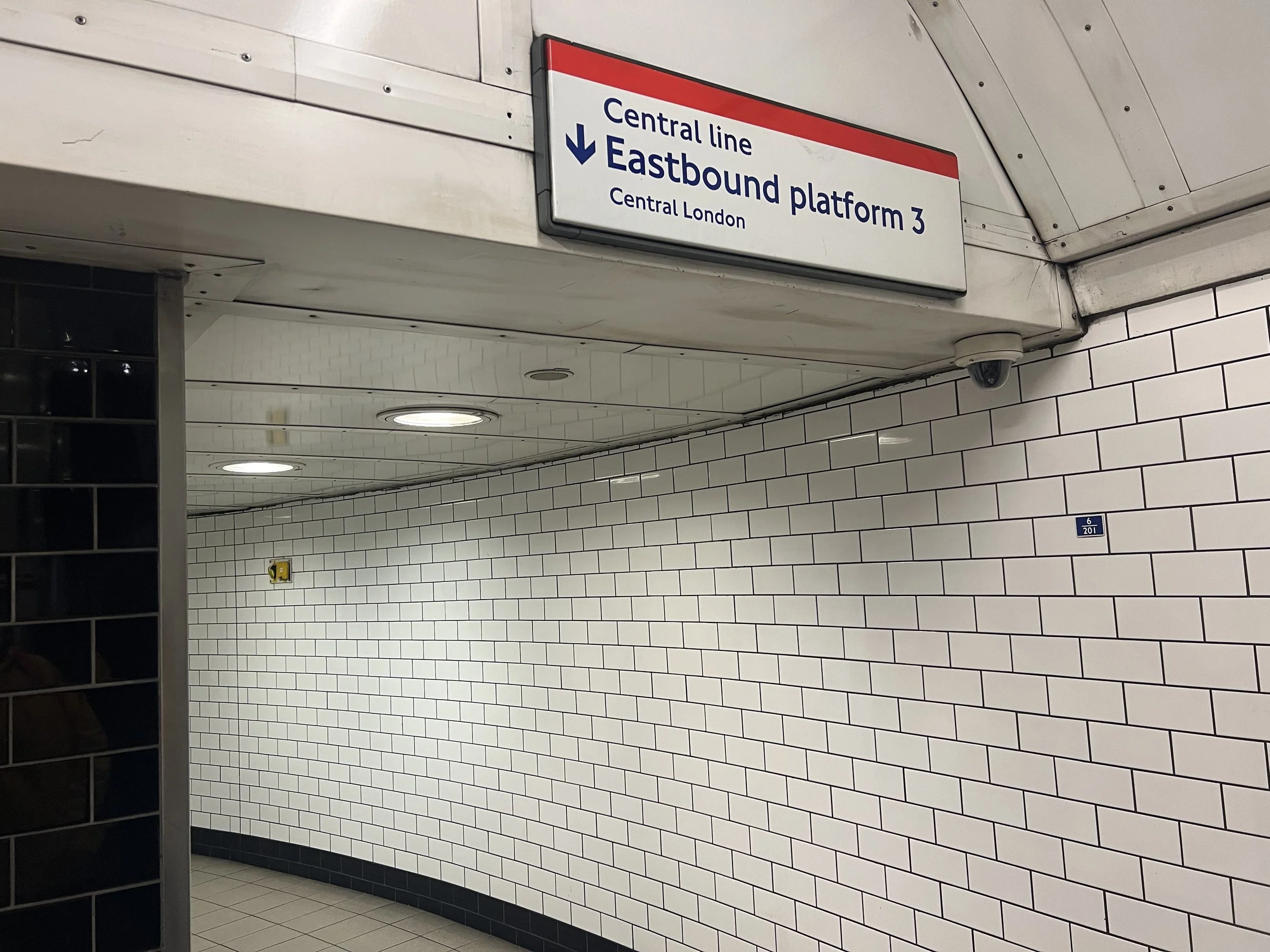 Sign in a subway station indicating the direction to Central Line, Eastbound platform 3, in Central London, with white tiled walls and ceiling lights.
