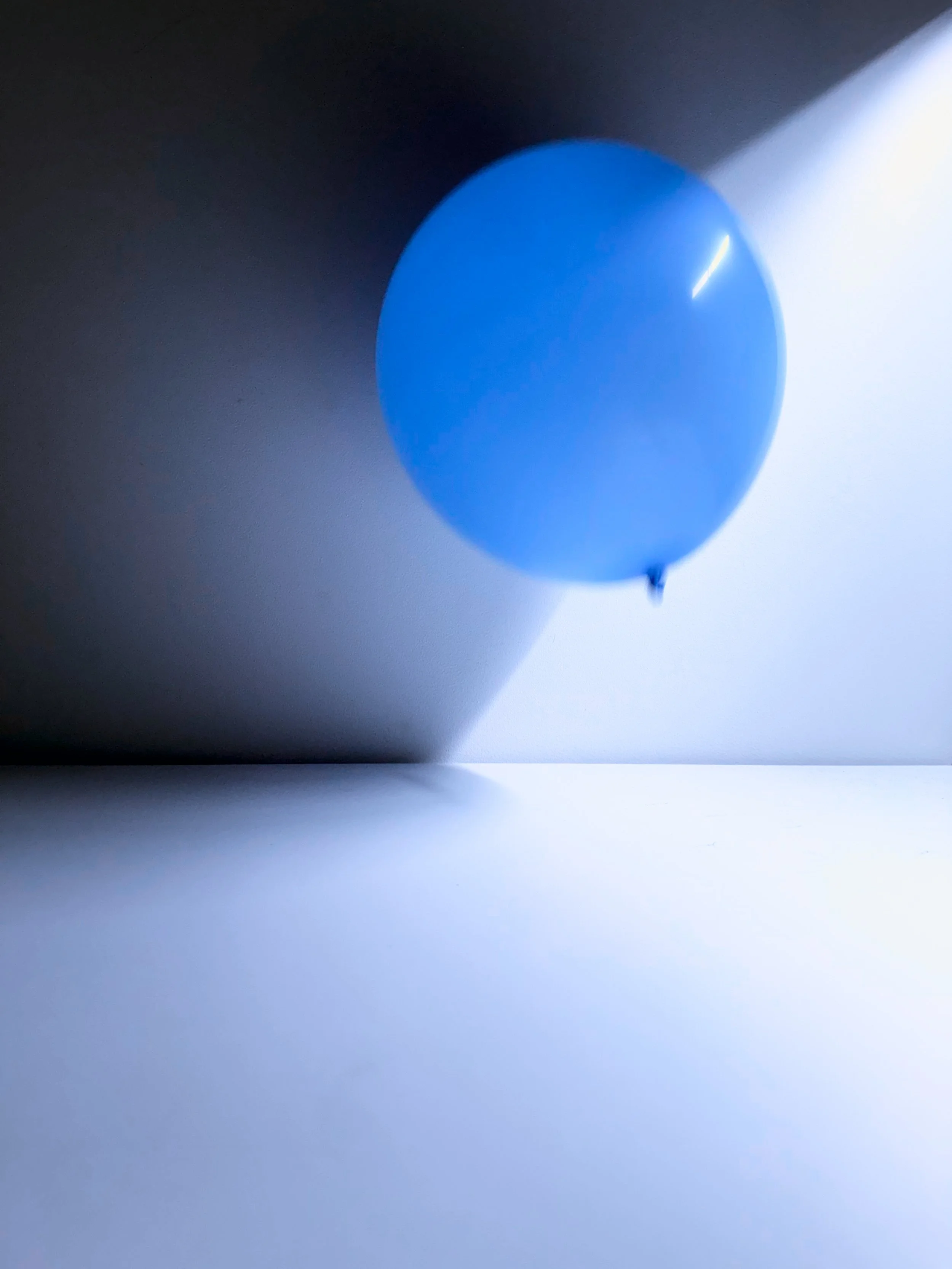 A blue balloon casting a shadow on a surface with a gradient of dark to light lighting.