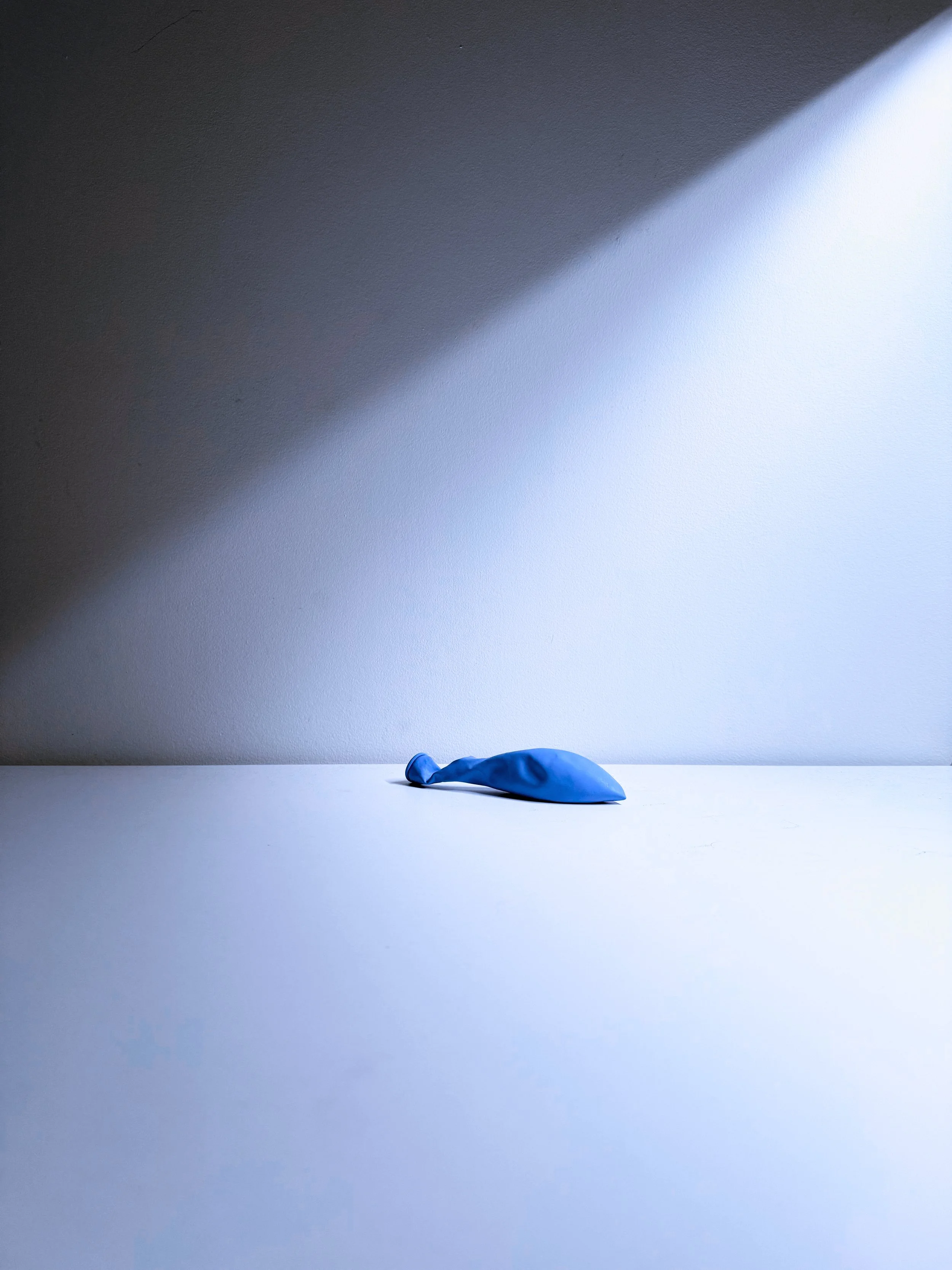 A blue balloon shaped like a balloon animal on a white surface, with a shadow cast on the wall in the background.