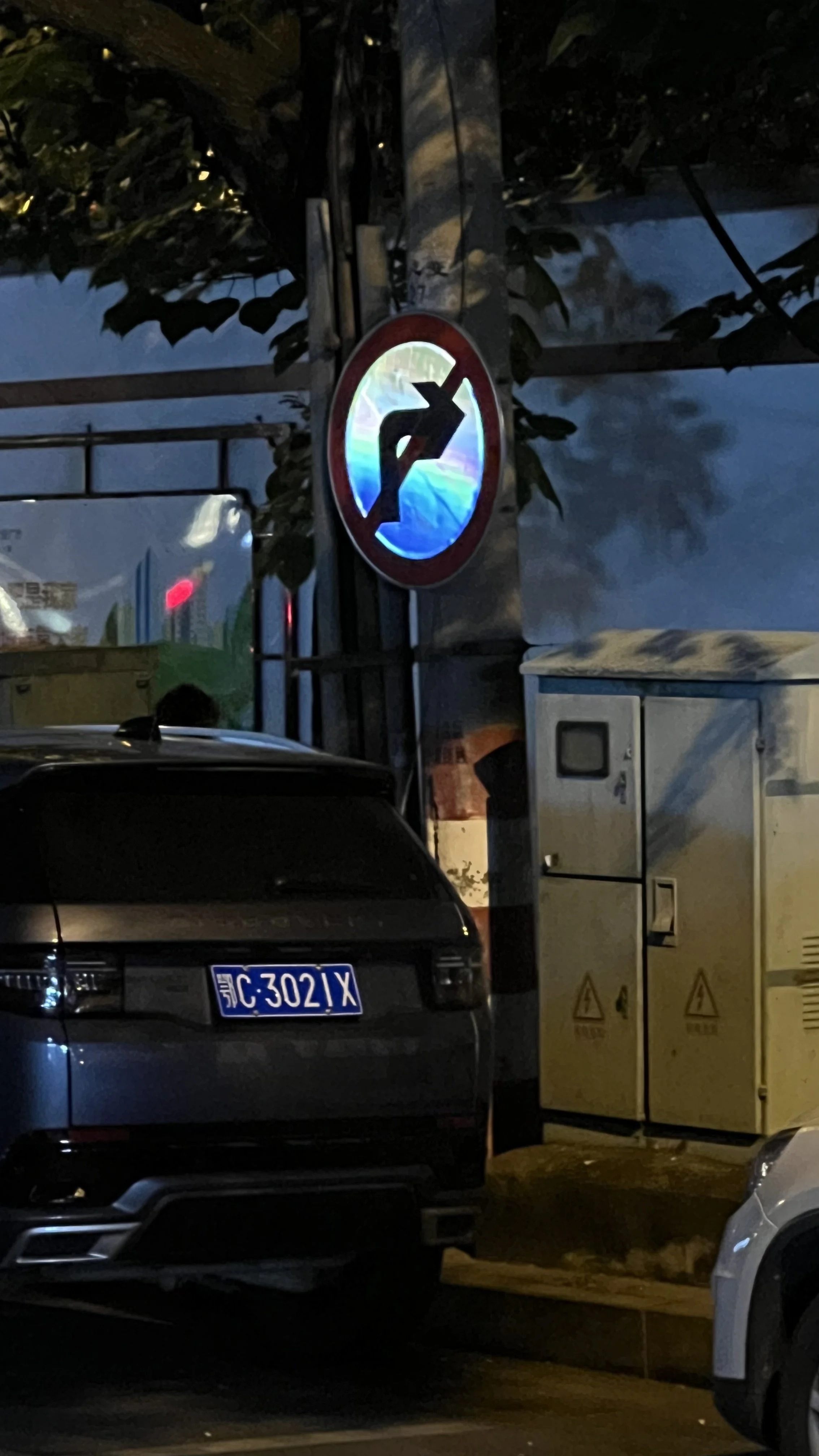 Nighttime scene showing a no-turn-on-red traffic sign. Cars are parked, and utility boxes are visible.