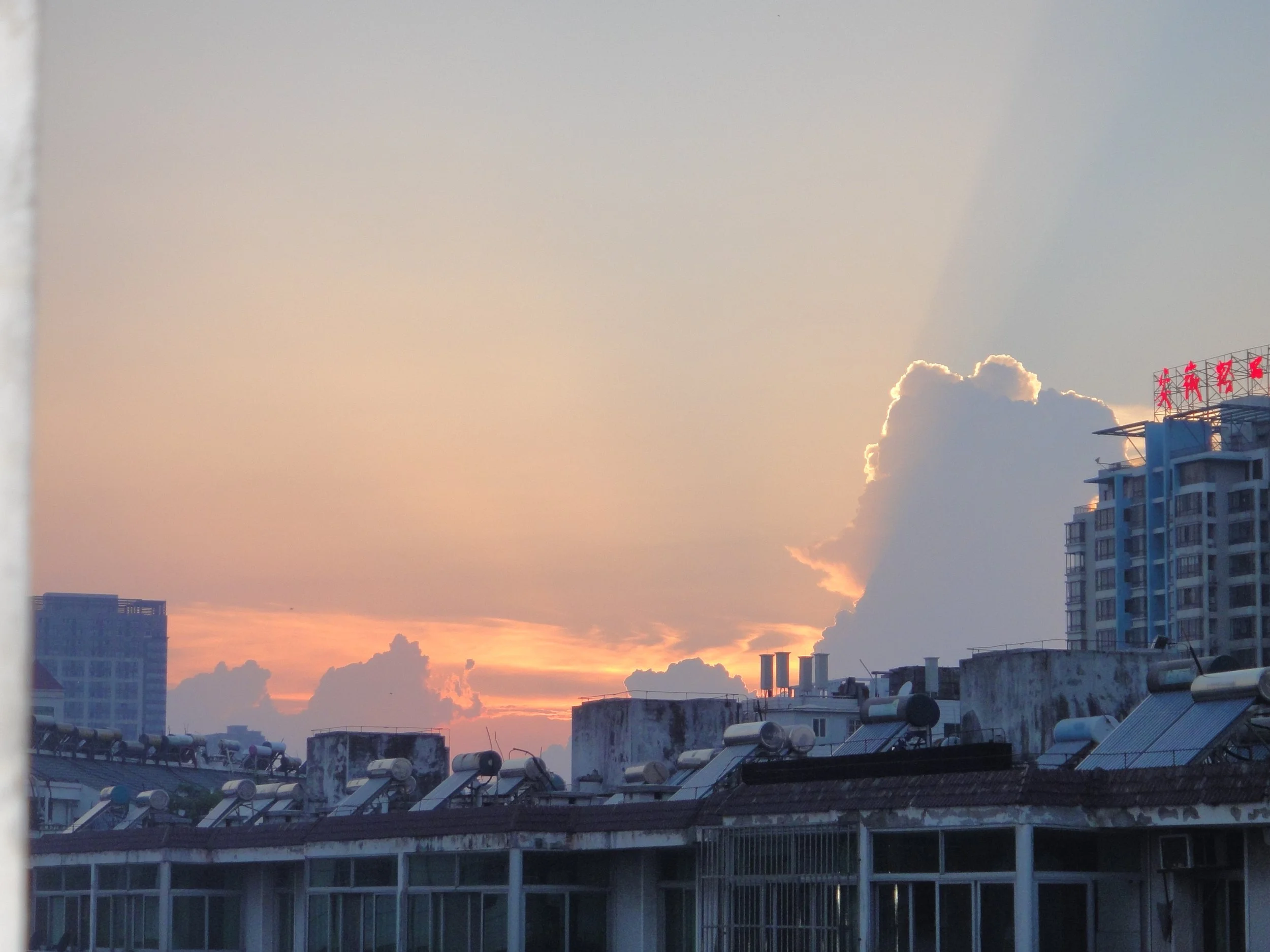 Sunset over a city skyline with clouds, skyscrapers, and rooftops with solar water heaters.
