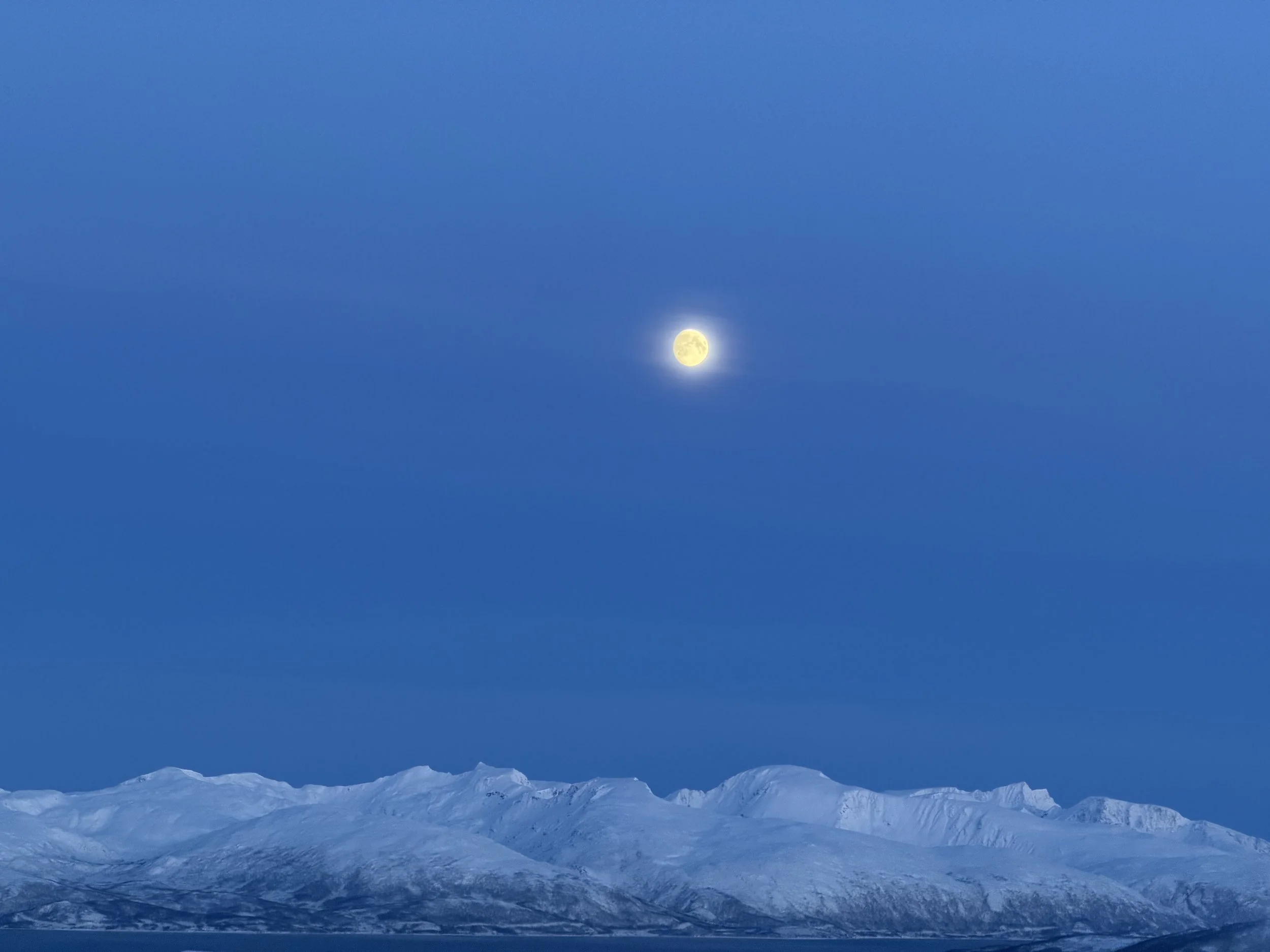 A snowy mountain range under a clear blue sky with the moon visible.