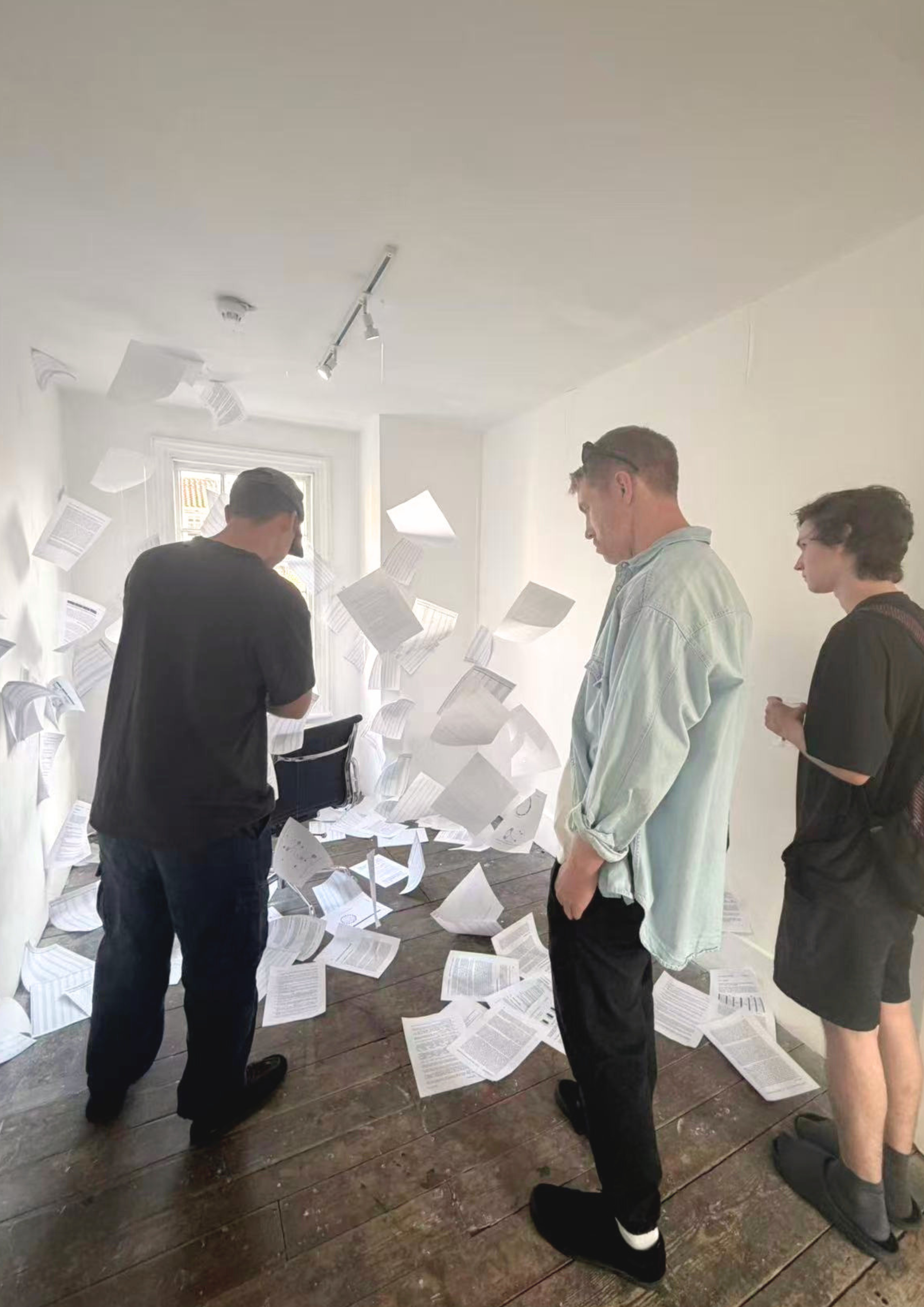 Four people standing in a room filled with flying papers and documents, with a window in the background.