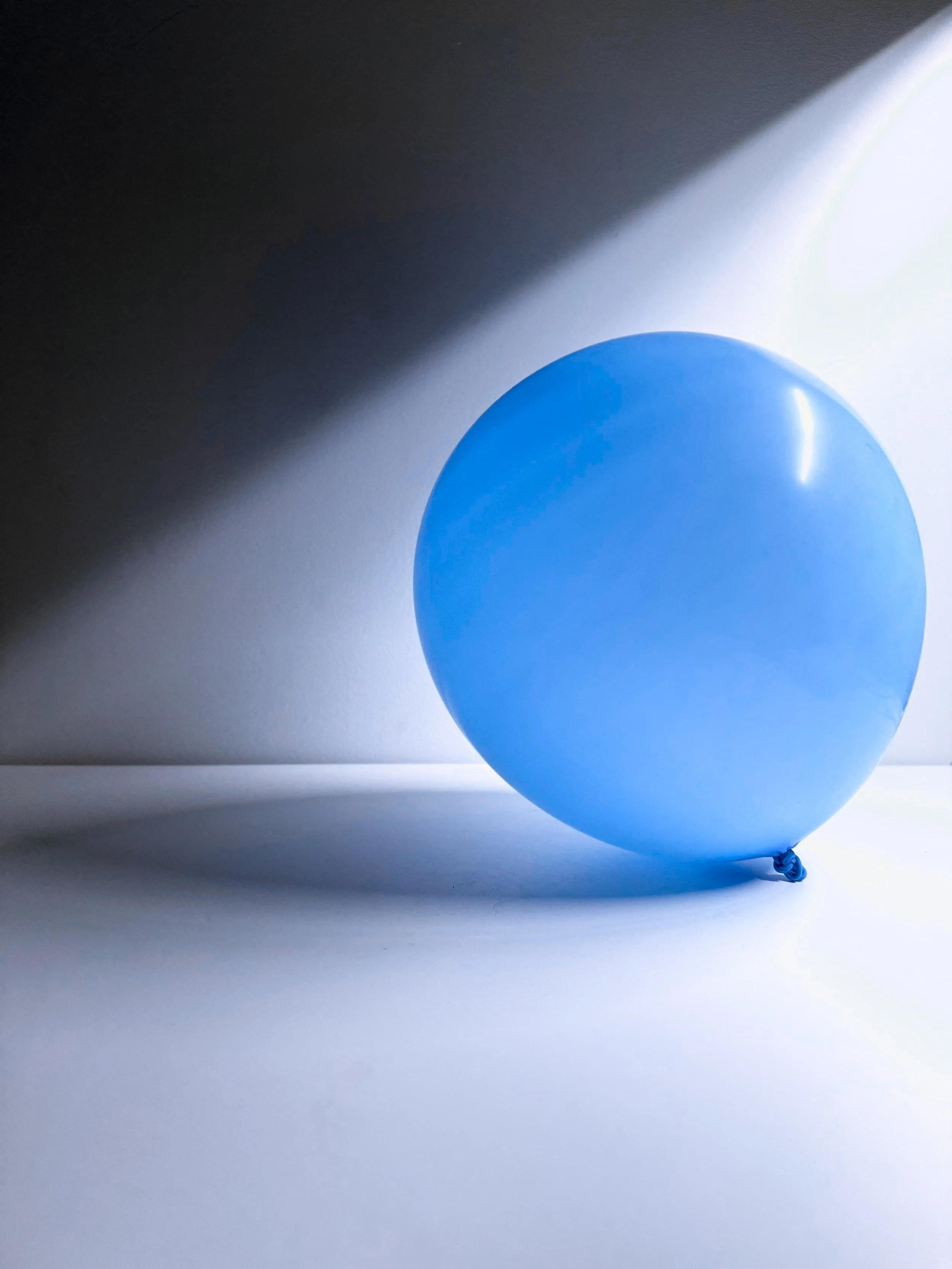 Blue balloon on a flat surface, casting a shadow on the white background.