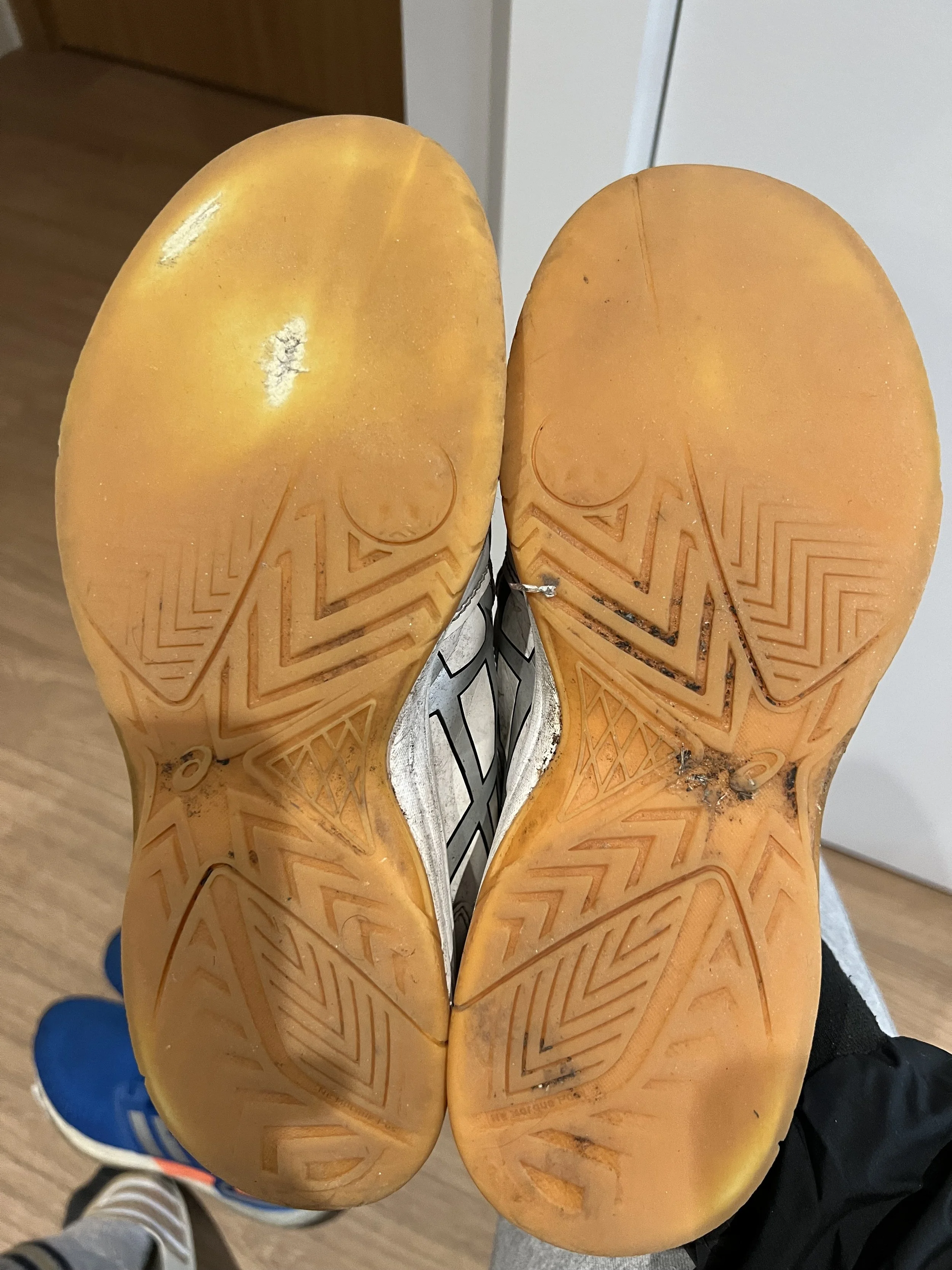 View of the soles of a pair of white athletic shoes with a yellowish sole, showing dirt and wear, and the brand name "VIBRAM" inscribed on the bottom.