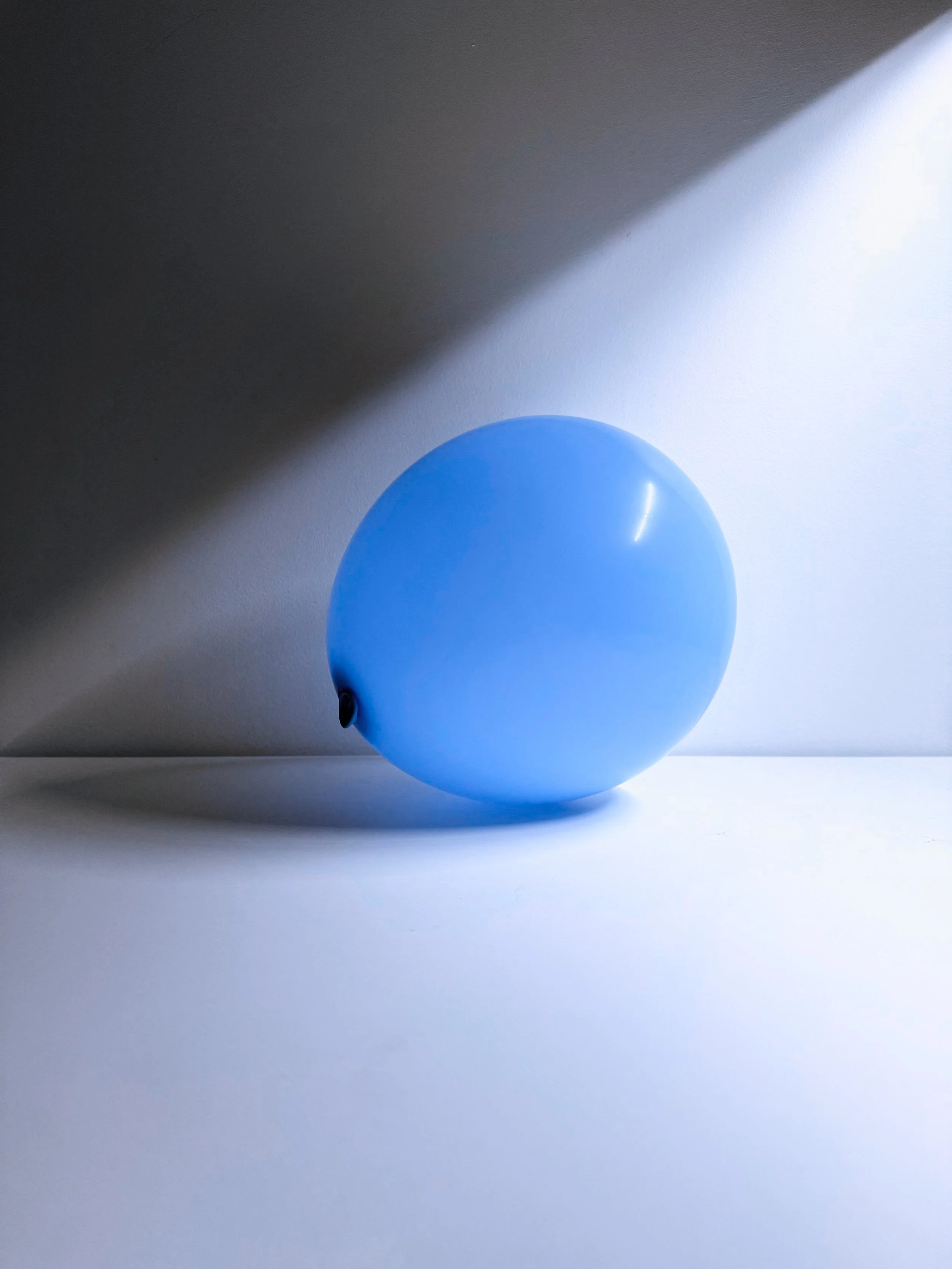 A blue balloon on a white surface, casting a shadow with a light source coming from the right side.