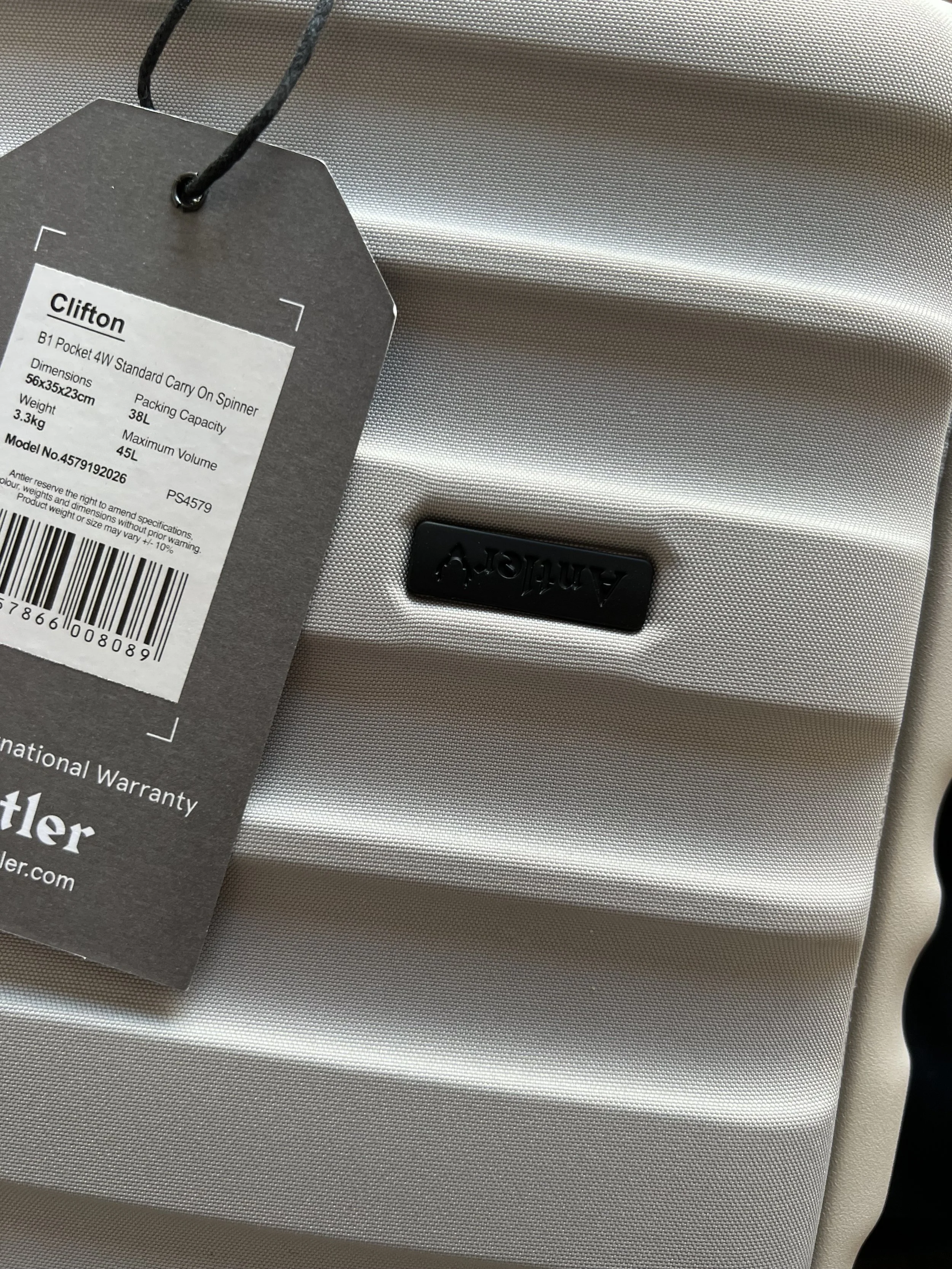 A silver Samsonite hard-shell carry-on suitcase with a black label that has product details attached, lying on a textured surface.