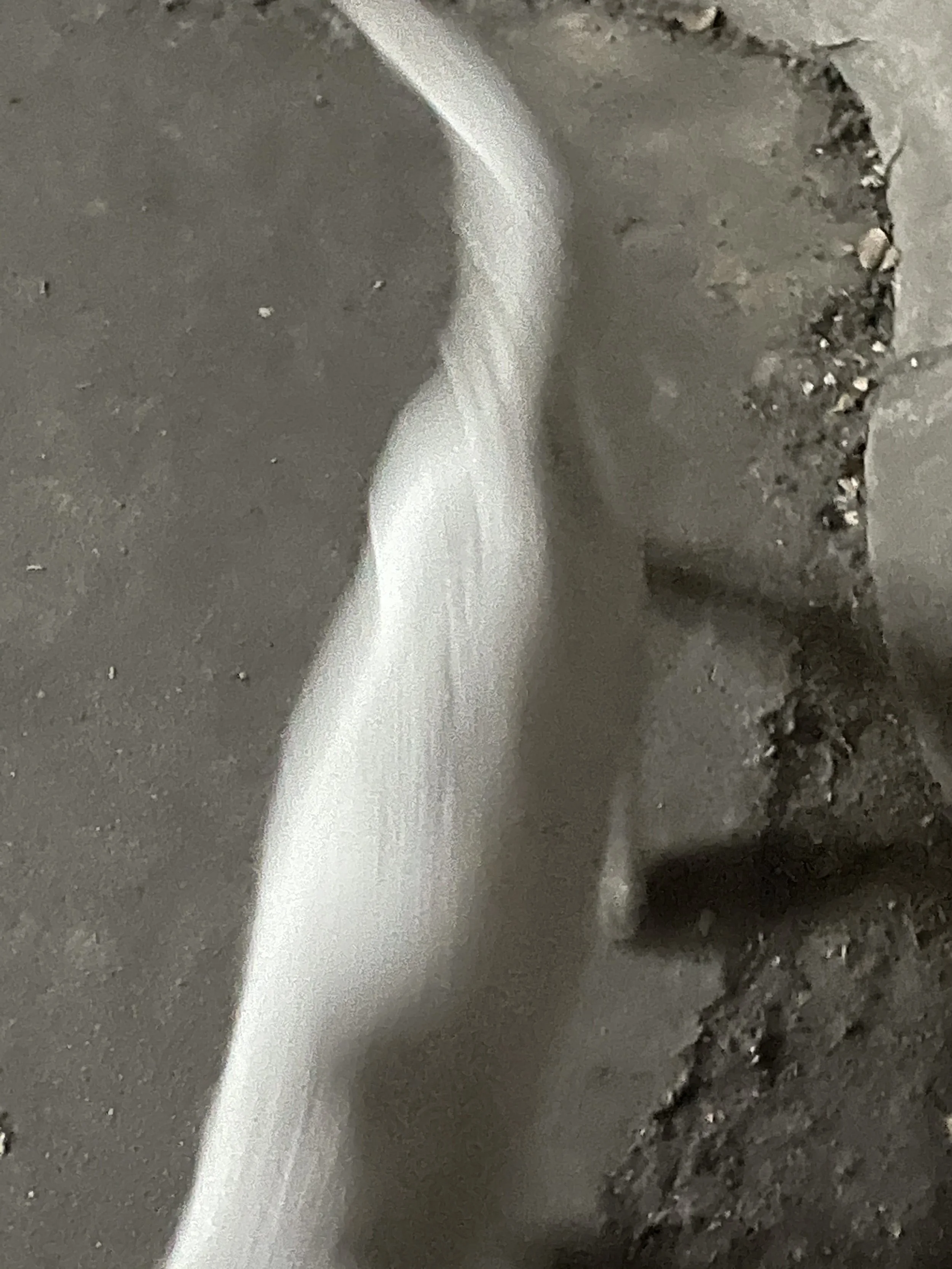 Close-up of a metal surface with a small stream of white liquid flowing over it, and some rough, uneven areas with small particles or debris.
