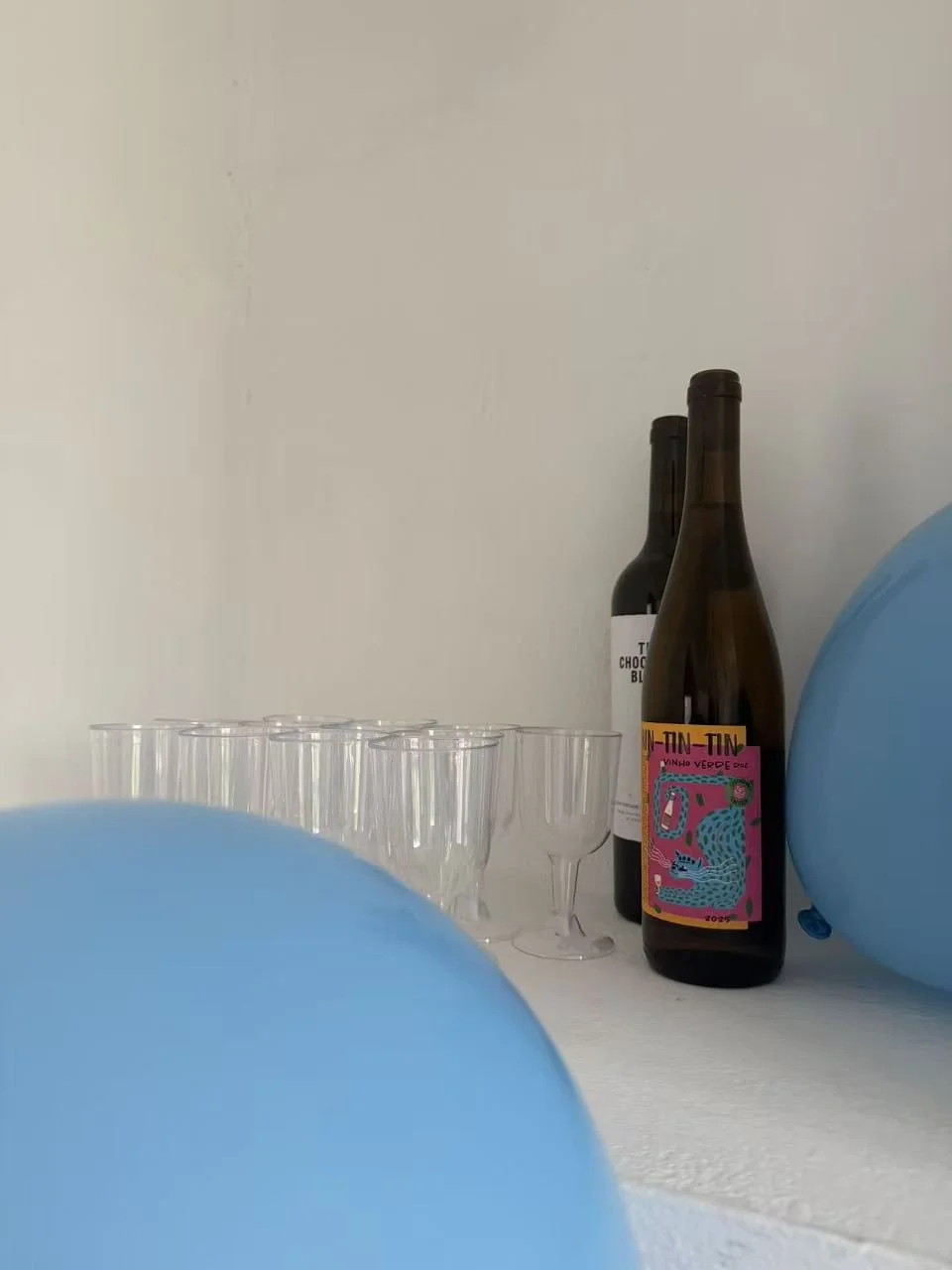 Two bottles of wine and several empty shot glasses on a table, with blue balloons partially visible in the foreground.