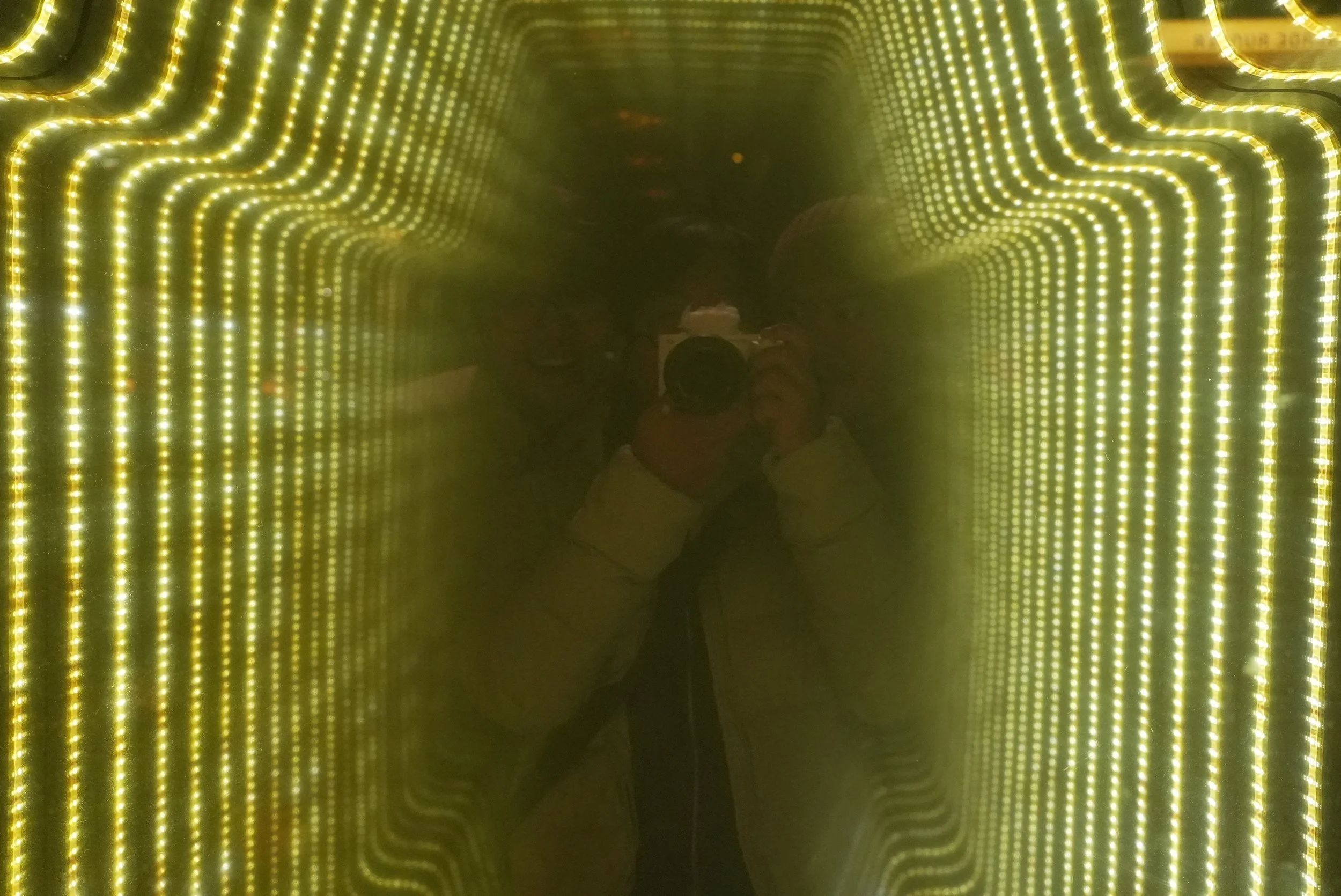 A person taking a photo of themselves in an illuminated tunnel with strip lights on the walls, ceiling, and floor.