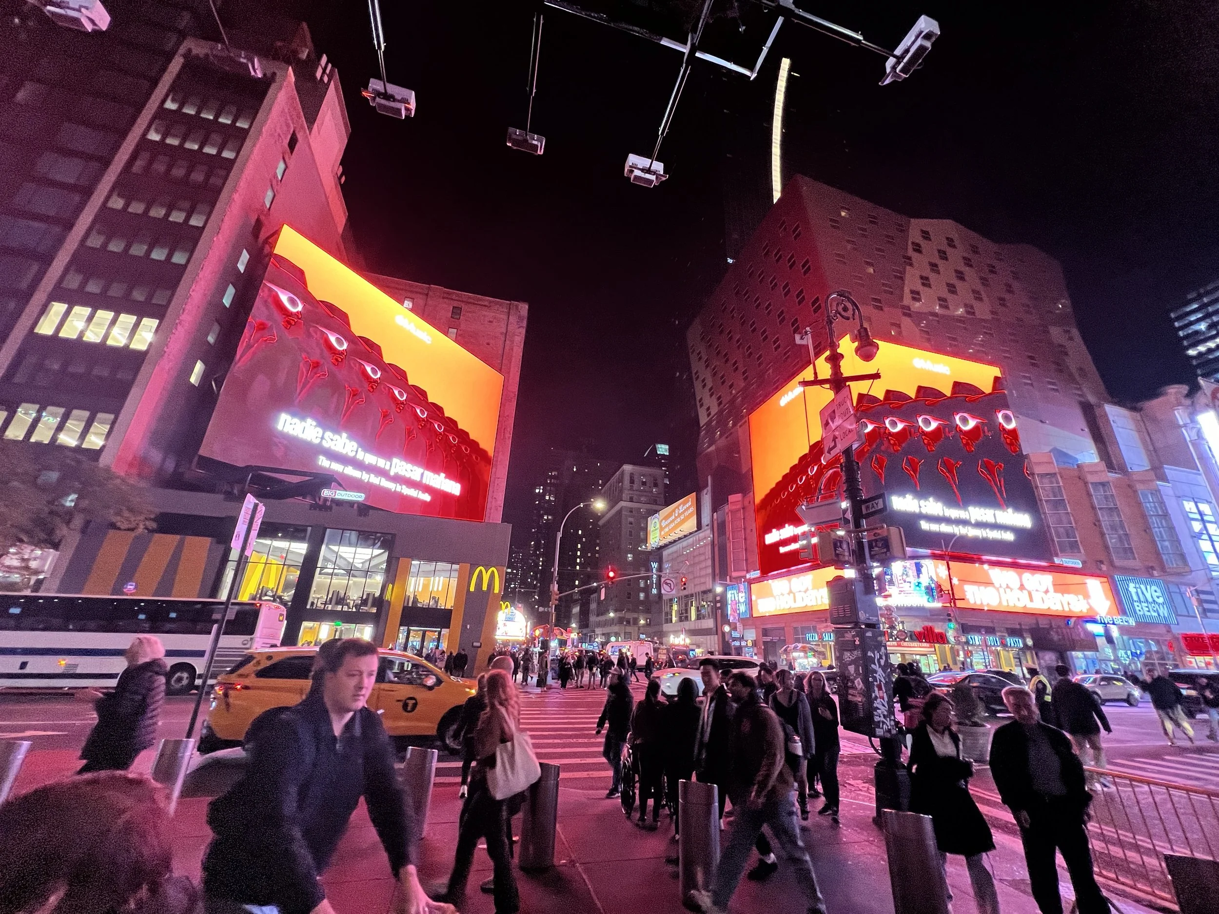 Nighttime city scene with illuminated billboards, tall buildings, and a busy crosswalk with pedestrians and vehicles.