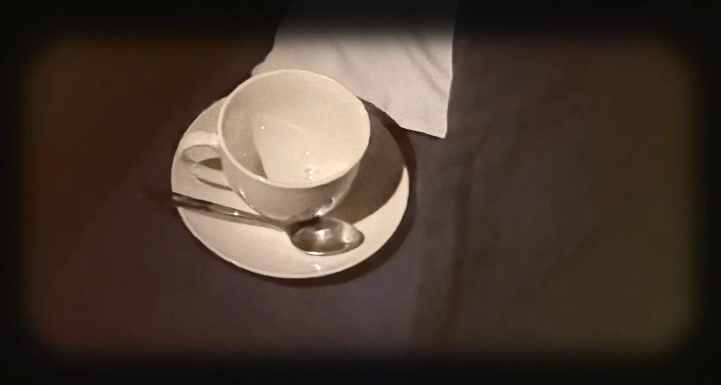 Empty white coffee cup on a saucer with a teaspoon and paper napkin on a dark table.