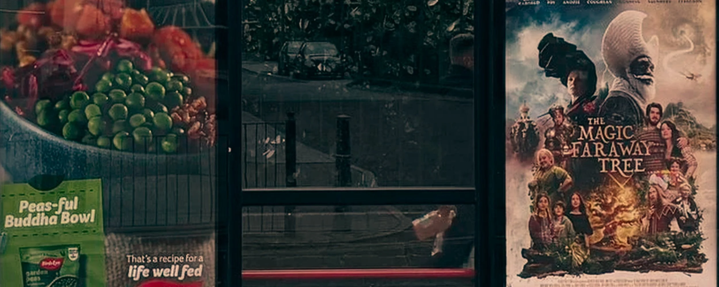 Grocery store window with grapes, a poster for the movie 'The Magic Faraway Tree,' and a green Peas-ful Buddha Bowl package.